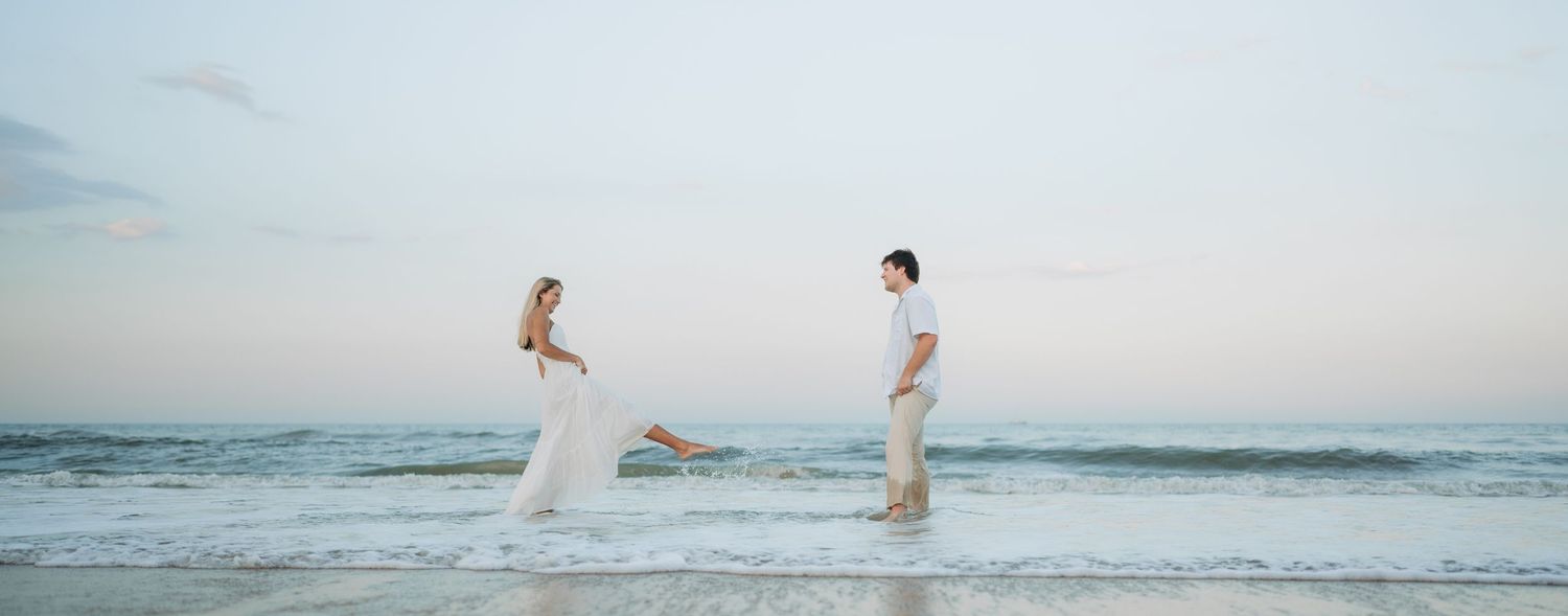 Couple jumping and playing together on a serene beach at dusk.