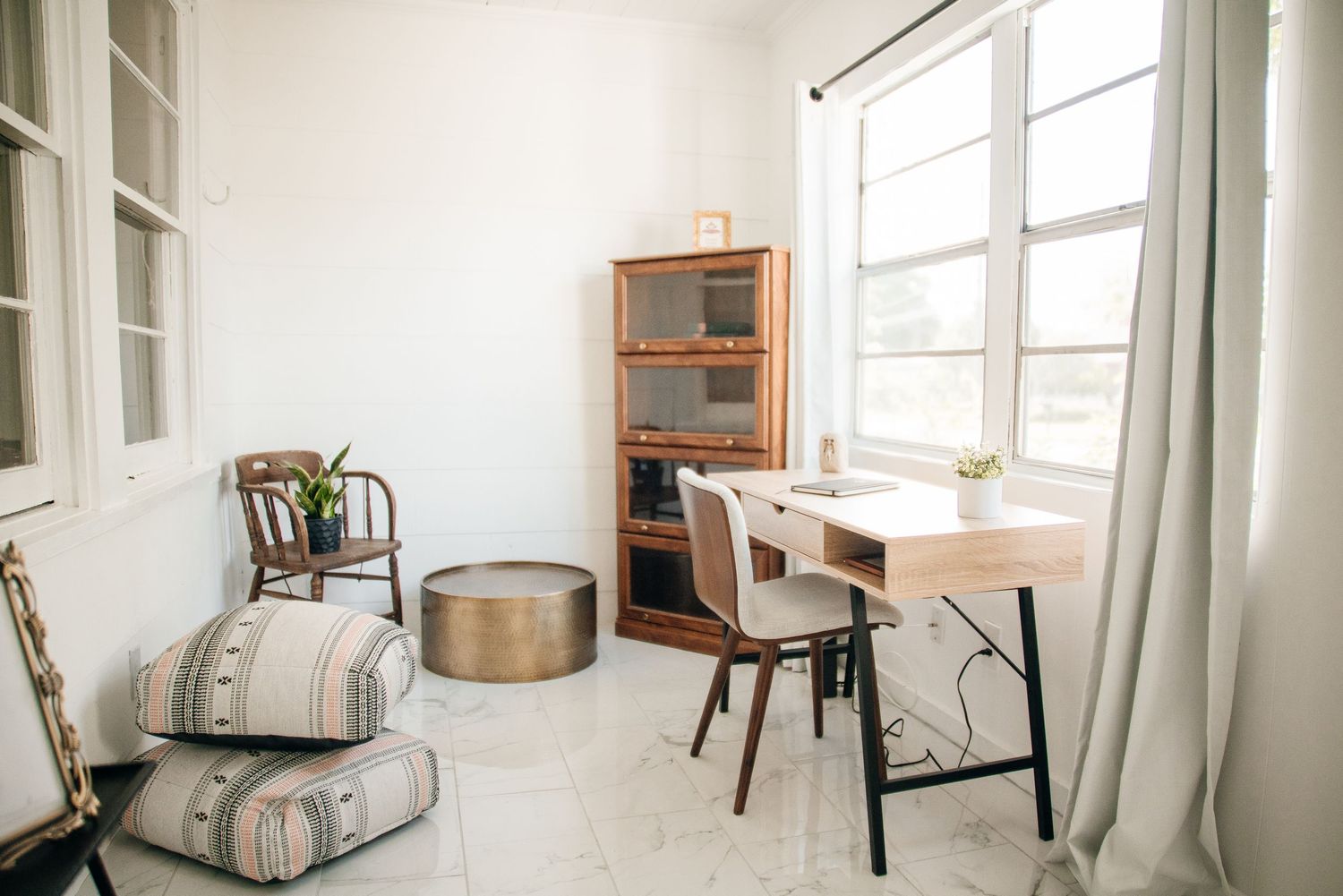 Bright minimalist home office with wooden desk, vintage bookcase, and floor cushions.
