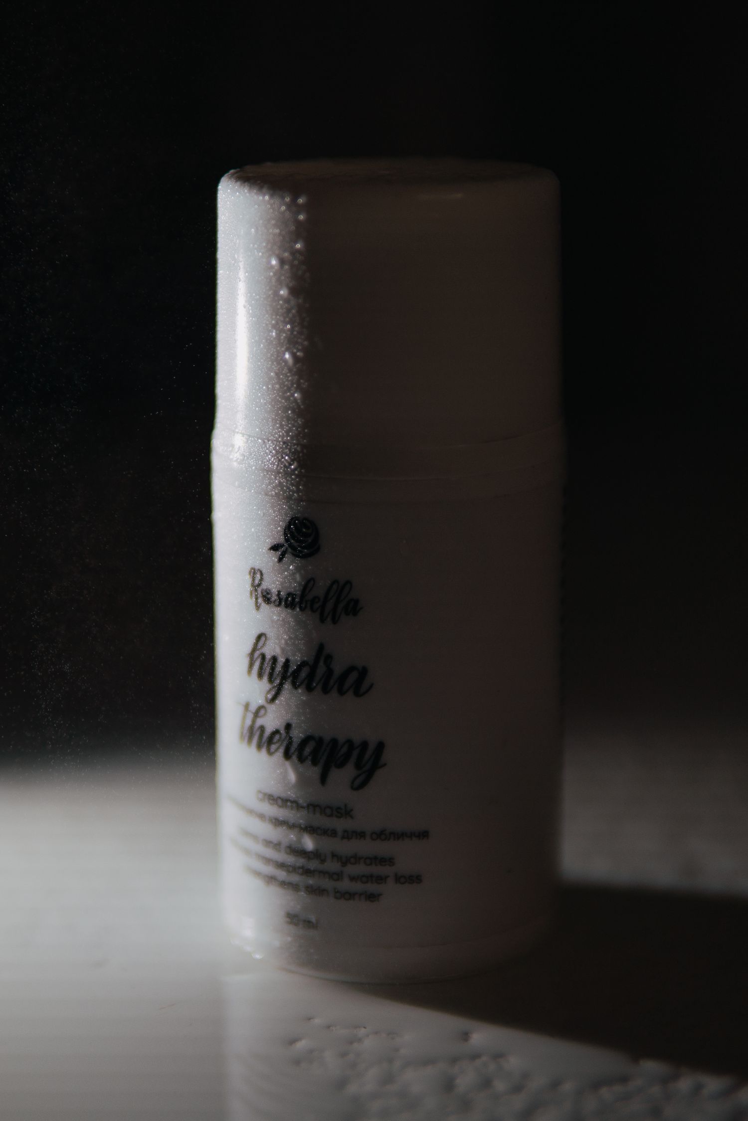 Rosabella Hydra Therapy moisturizing cream bottle with water droplets on dark background.