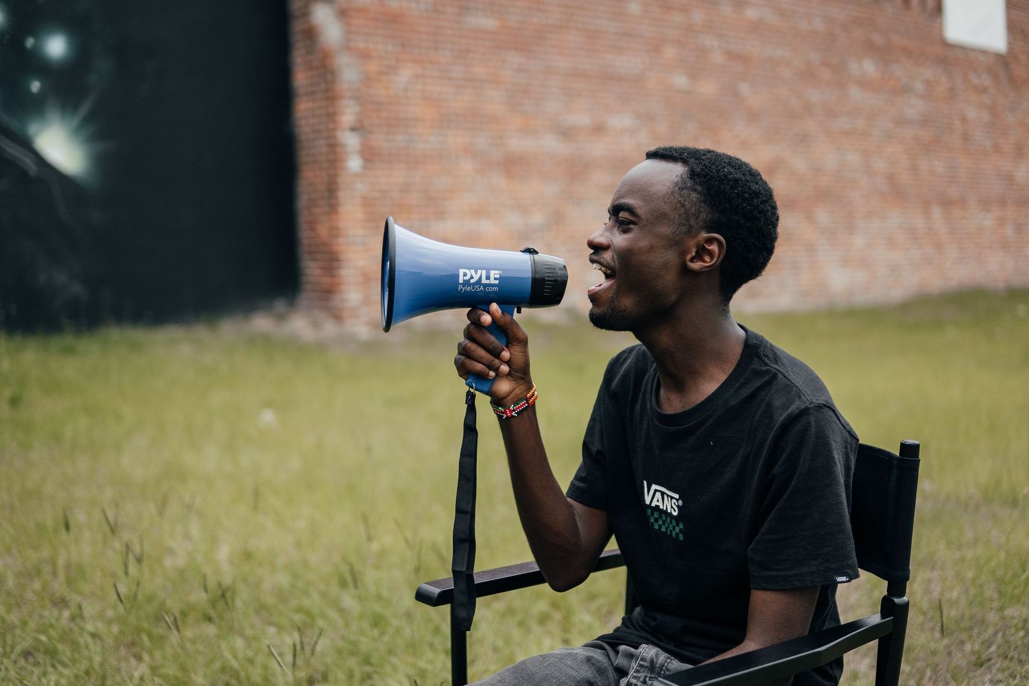 Person speaking through a megaphone while seated in front of brick wall.