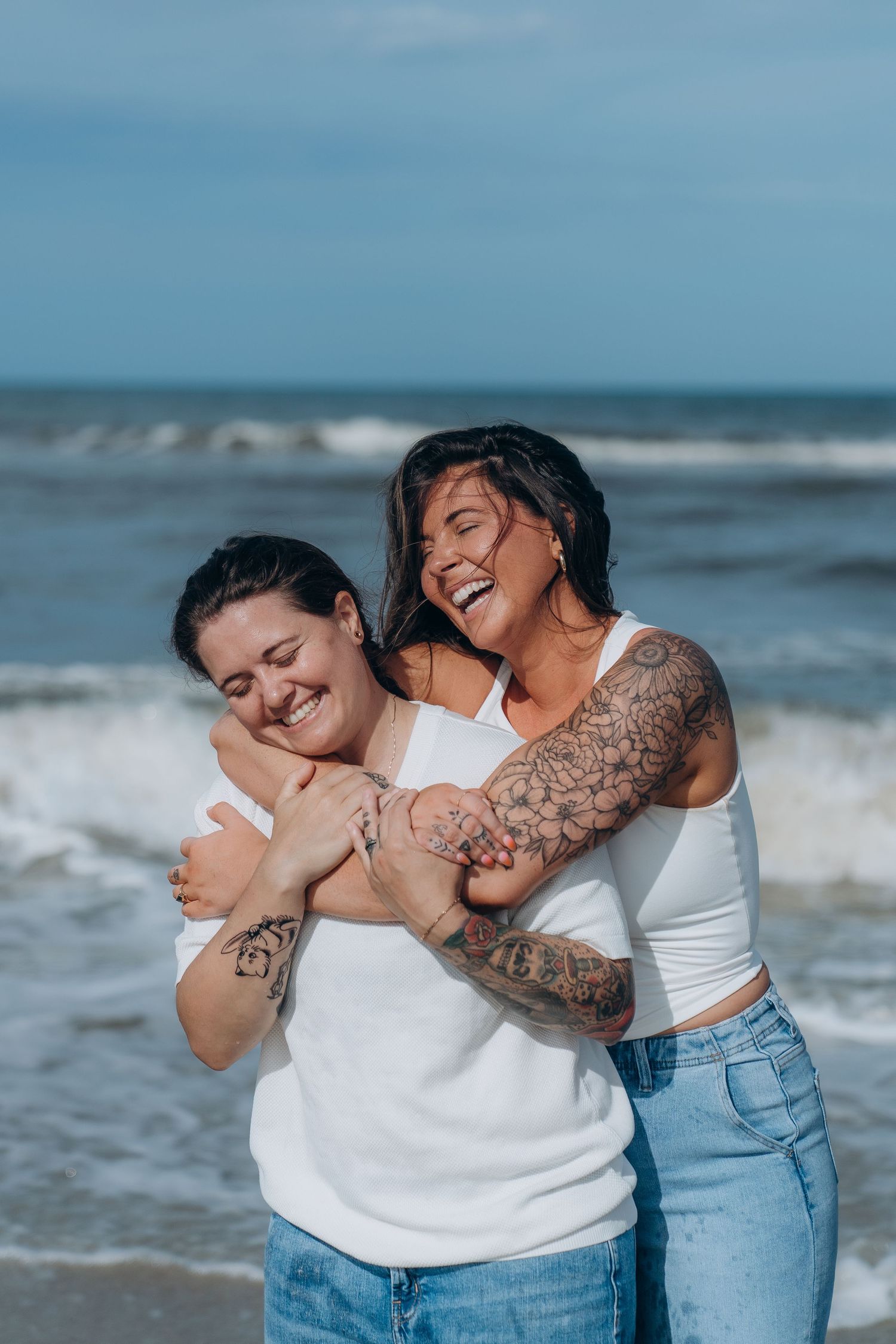 Two people share an intimate moment on a beach with crashing waves behind them.