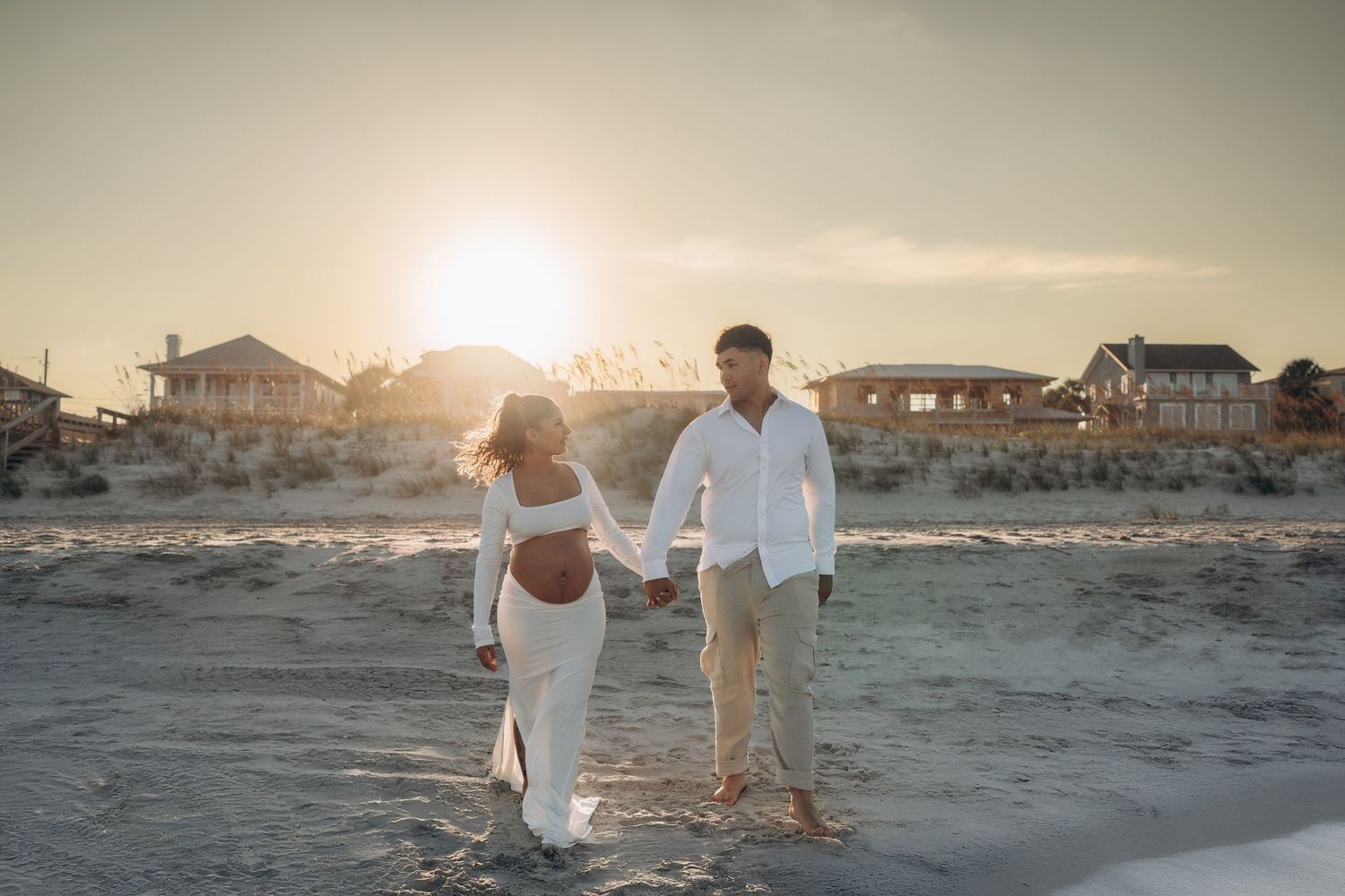 Golden hour beach scene with silhouettes walking along the shore near beachfront houses.