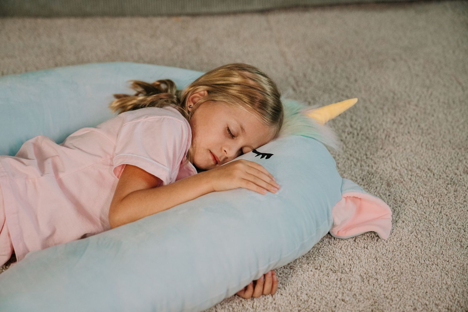 Girl sleeping on a teal unicorn body pillow on carpet floor.