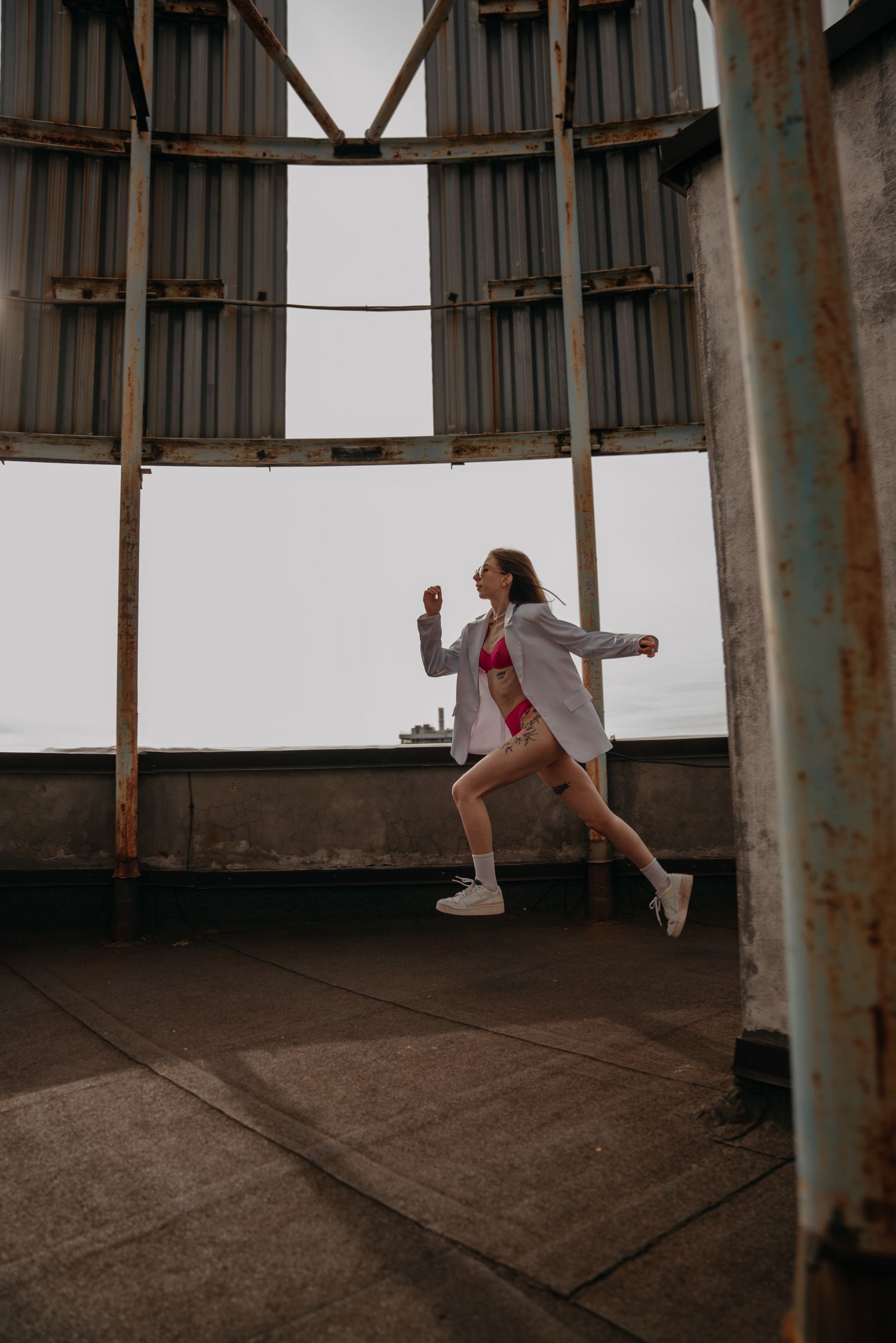 Dynamic shot of woman running in pink bikini and white shirt inside industrial rooftop structure.