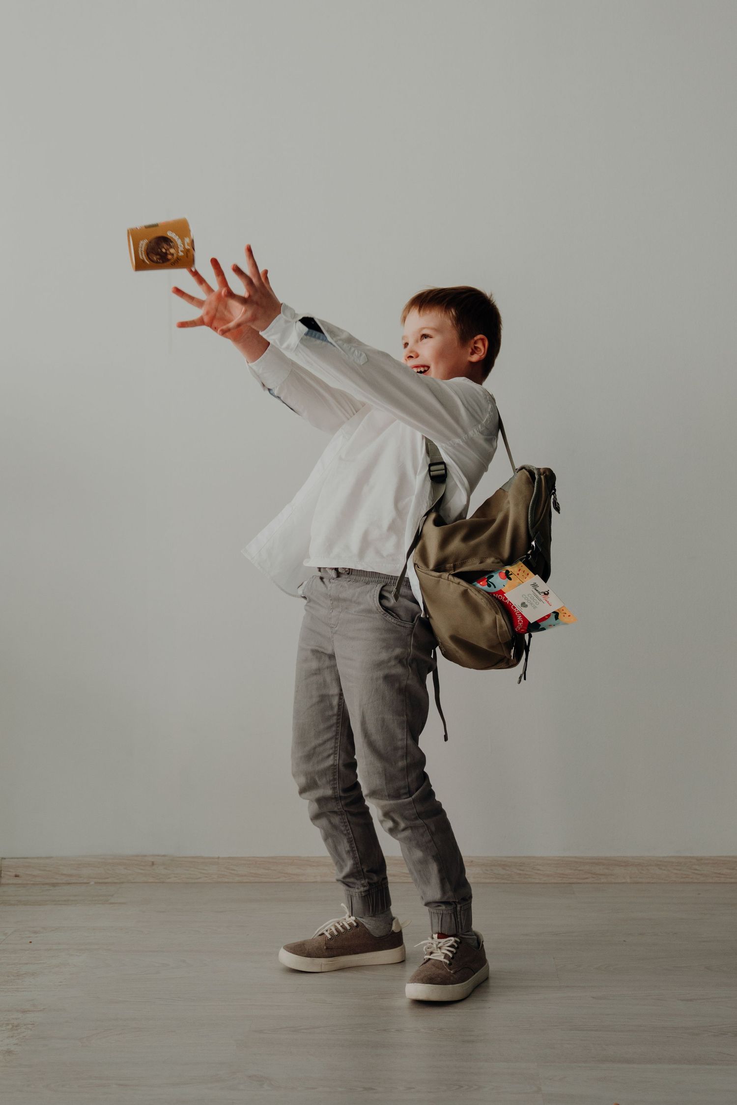 Young boy with backpack reaching out to catch a trading card against a light gray wall.