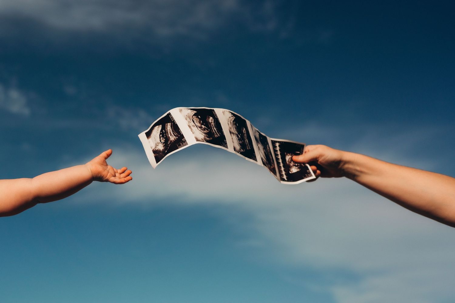 Two hands holding a strip of photo negatives against a blue sky with clouds.