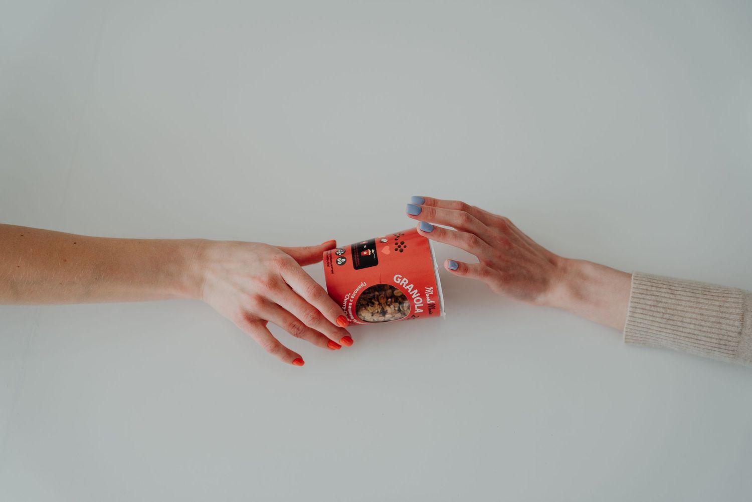 Two hands exchanging a small red gift box on a white background, with red and blue nail polish.