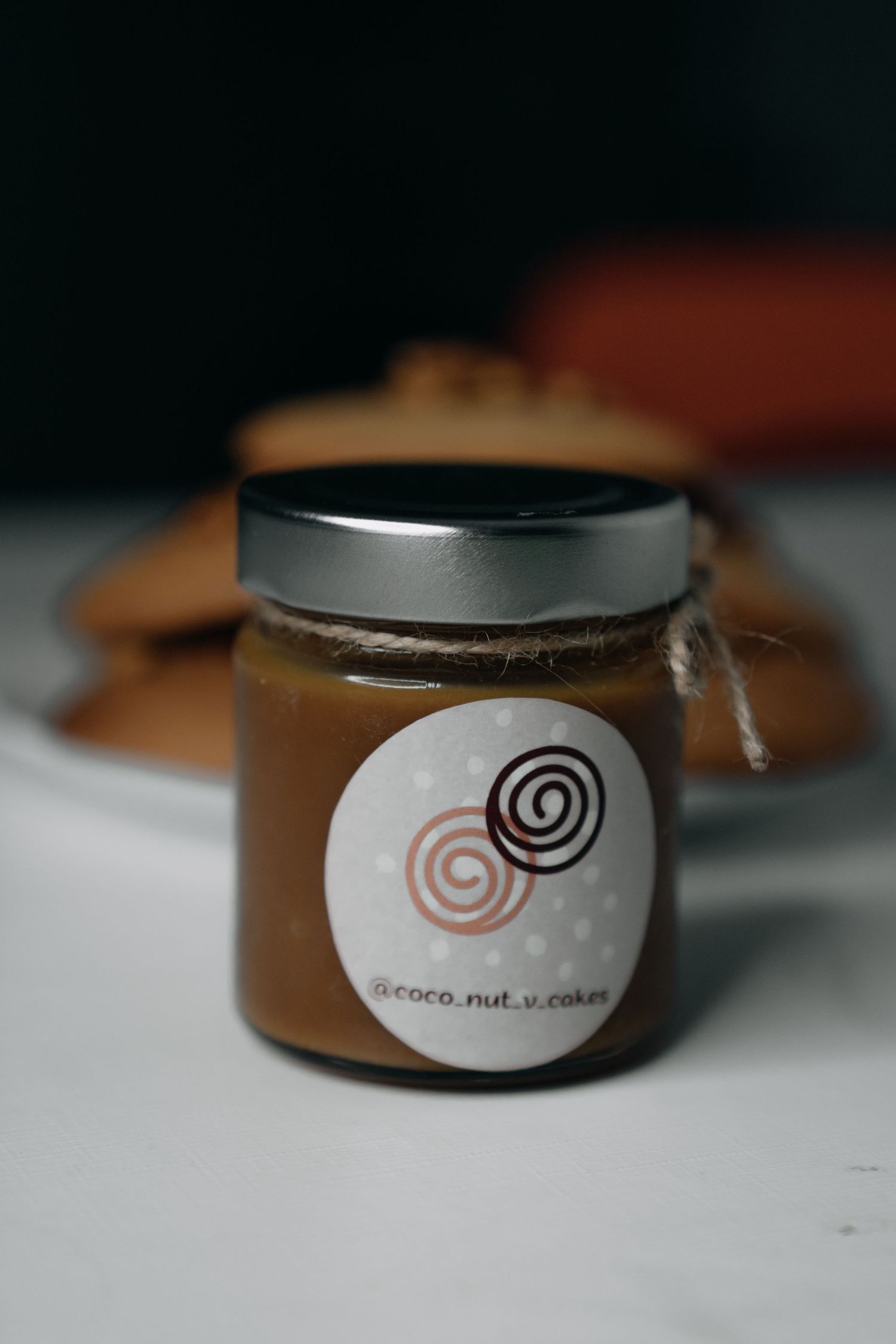 Small jar of caramel spread with coco.nut.v.cakes label on a white surface.