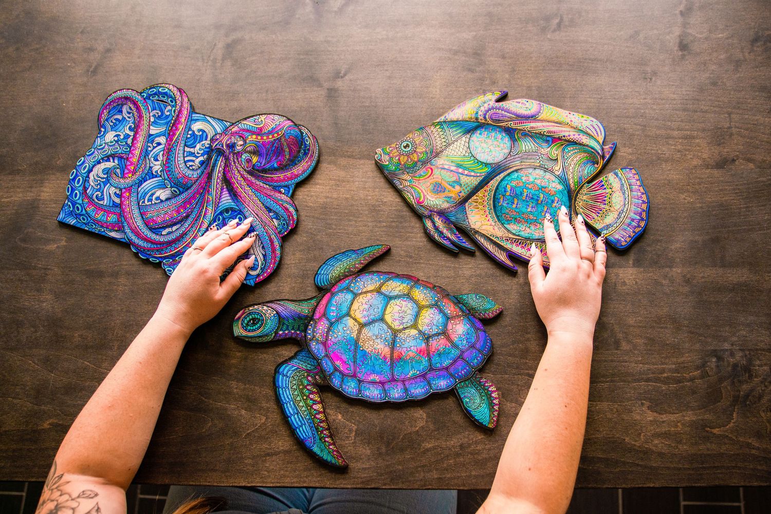 Hands assembling colorful wooden animal puzzles of an octopus, fish, and turtle on a wooden table.