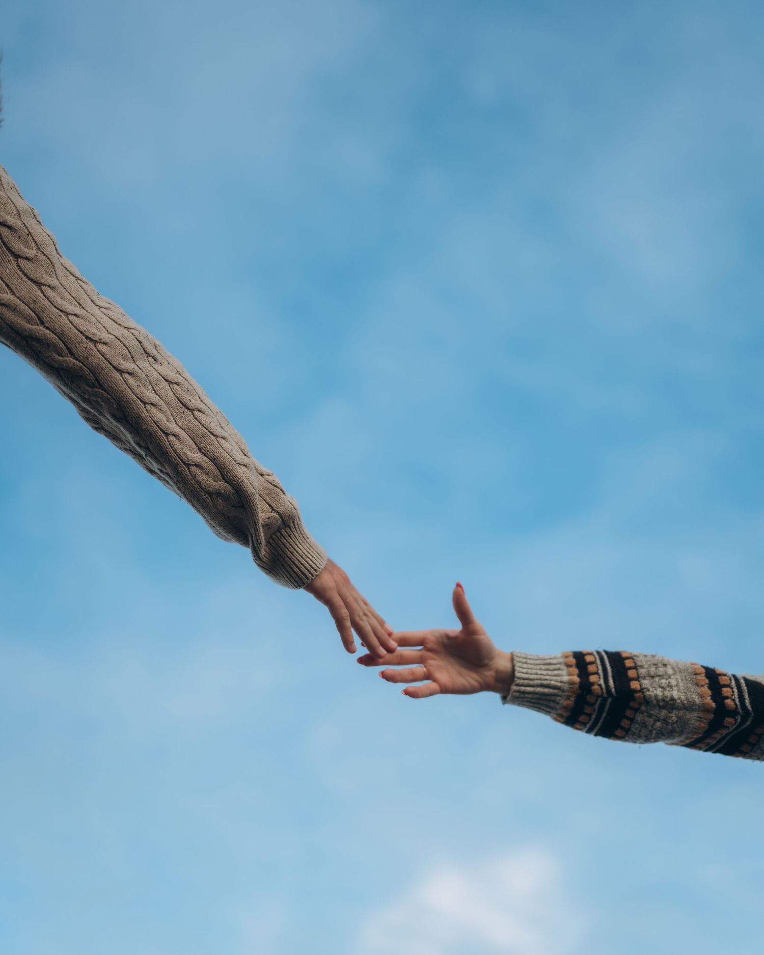 Hands reaching towards a bright blue sky with bracelets and jewelry visible.