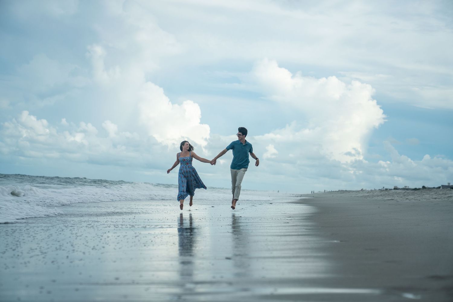 Two people walk hand in hand along a misty beach shoreline at sunset creating silhouettes against the water.