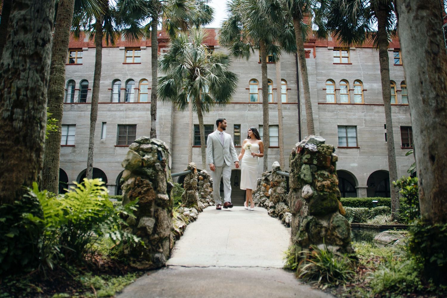 A series of connected archways and stone buildings with palm trees and landscaping at a historic Spanish colonial site.
