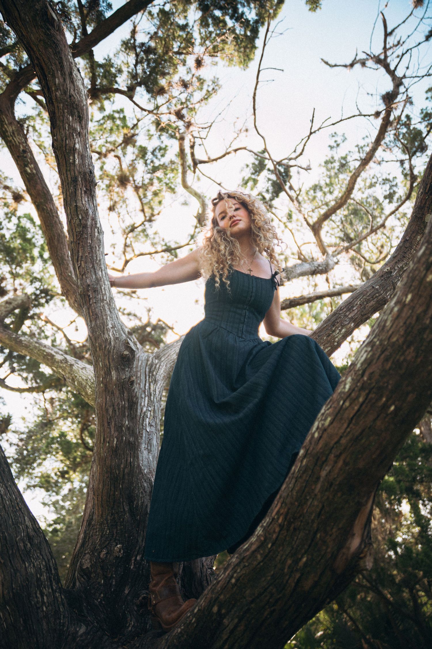 Adventurous pose while climbing a large tree in a flowing navy dress.