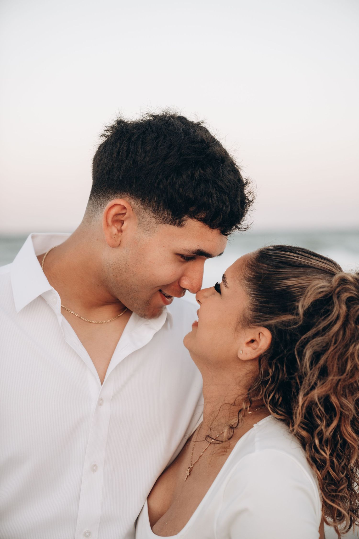 Close-up portraits of a couple in white clothing sharing romantic moments on the beach.