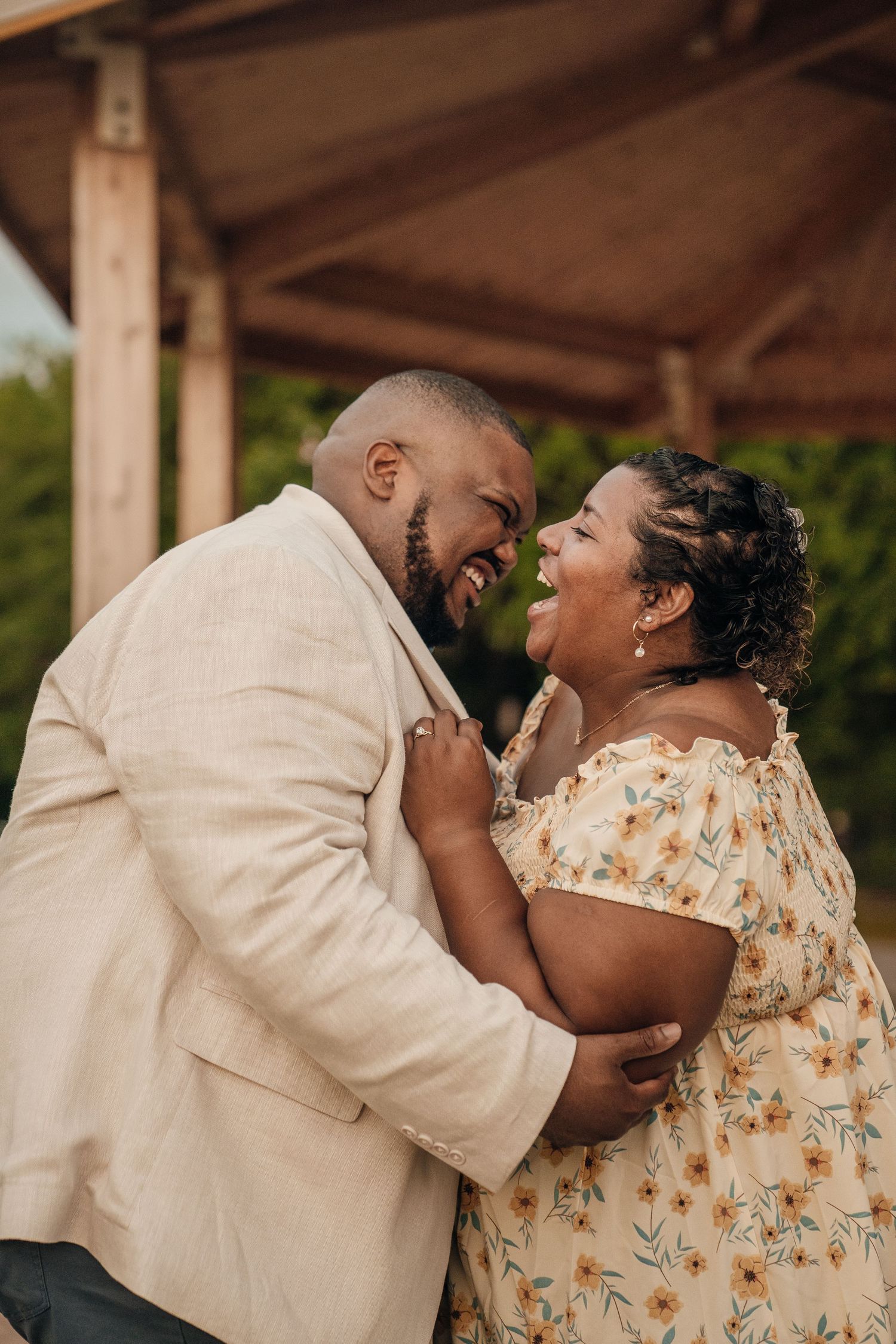 A couple shares a joyful laugh under a wooden pavilion.