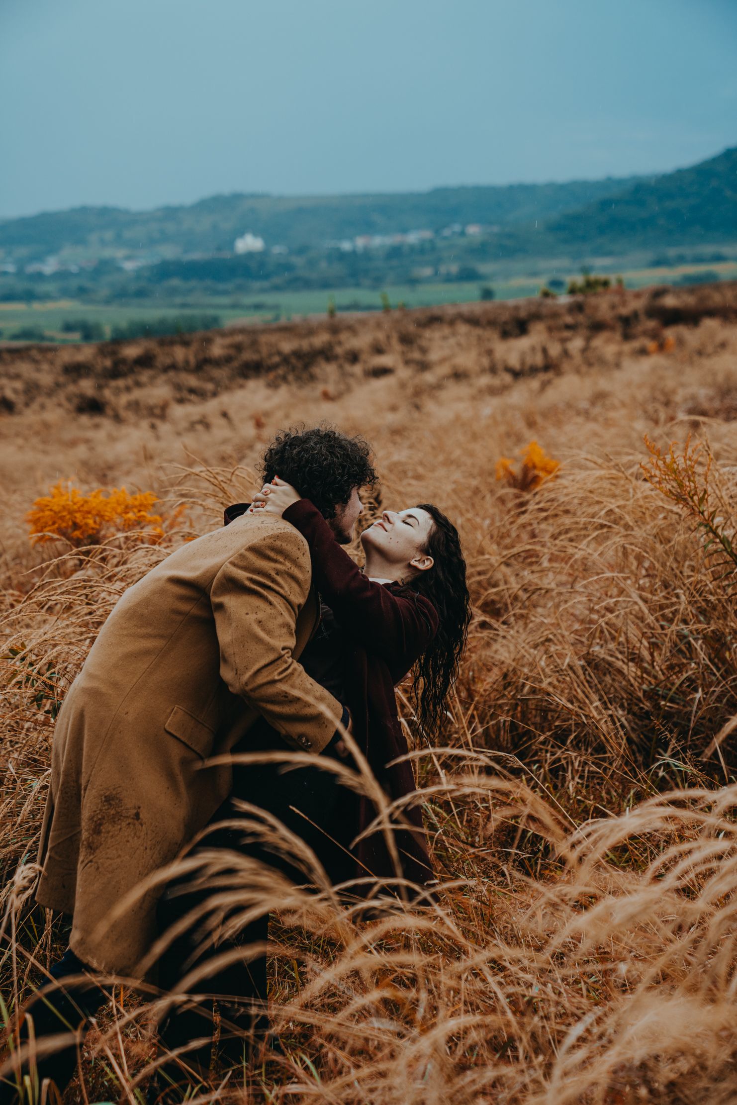 Romantic couple sharing an intimate moment in a golden field of tall grass at sunset.