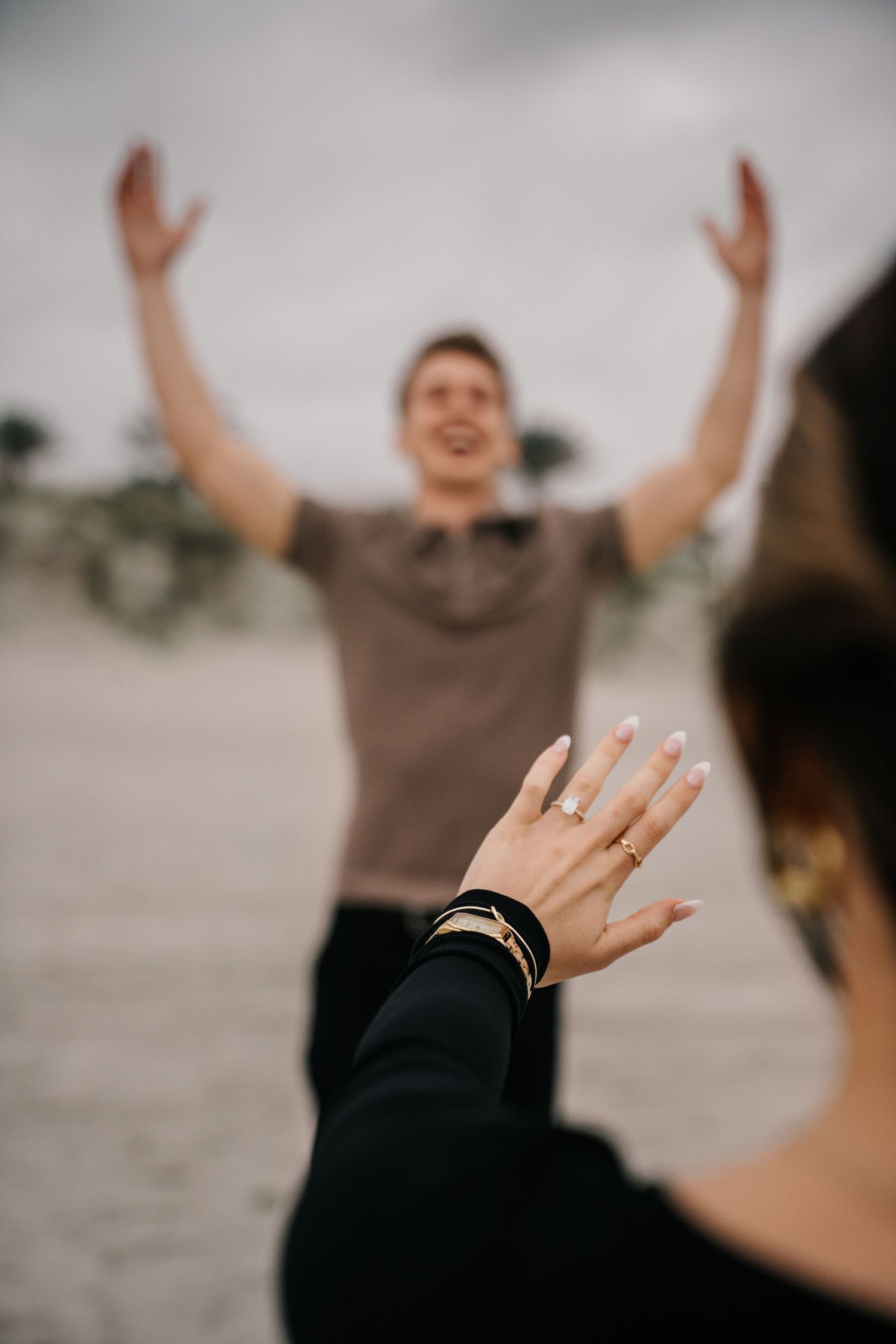 A close-up of hands raised in celebration showing an engagement ring on the beach.