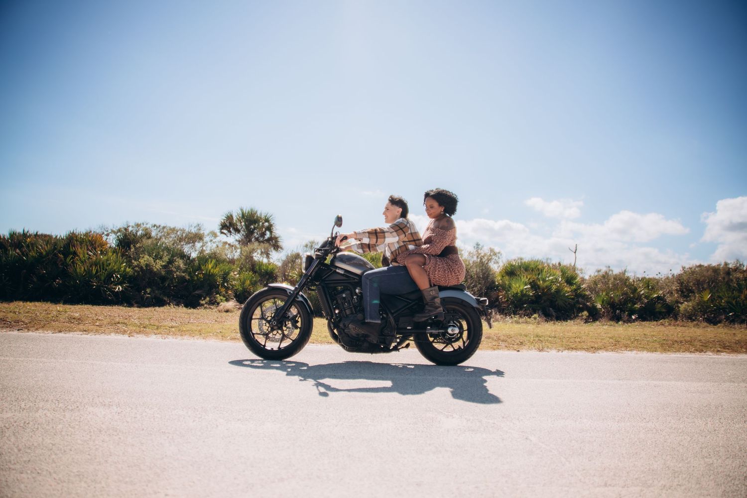 A sleek black motorcycle on an open road against a bright blue sky with white clouds.