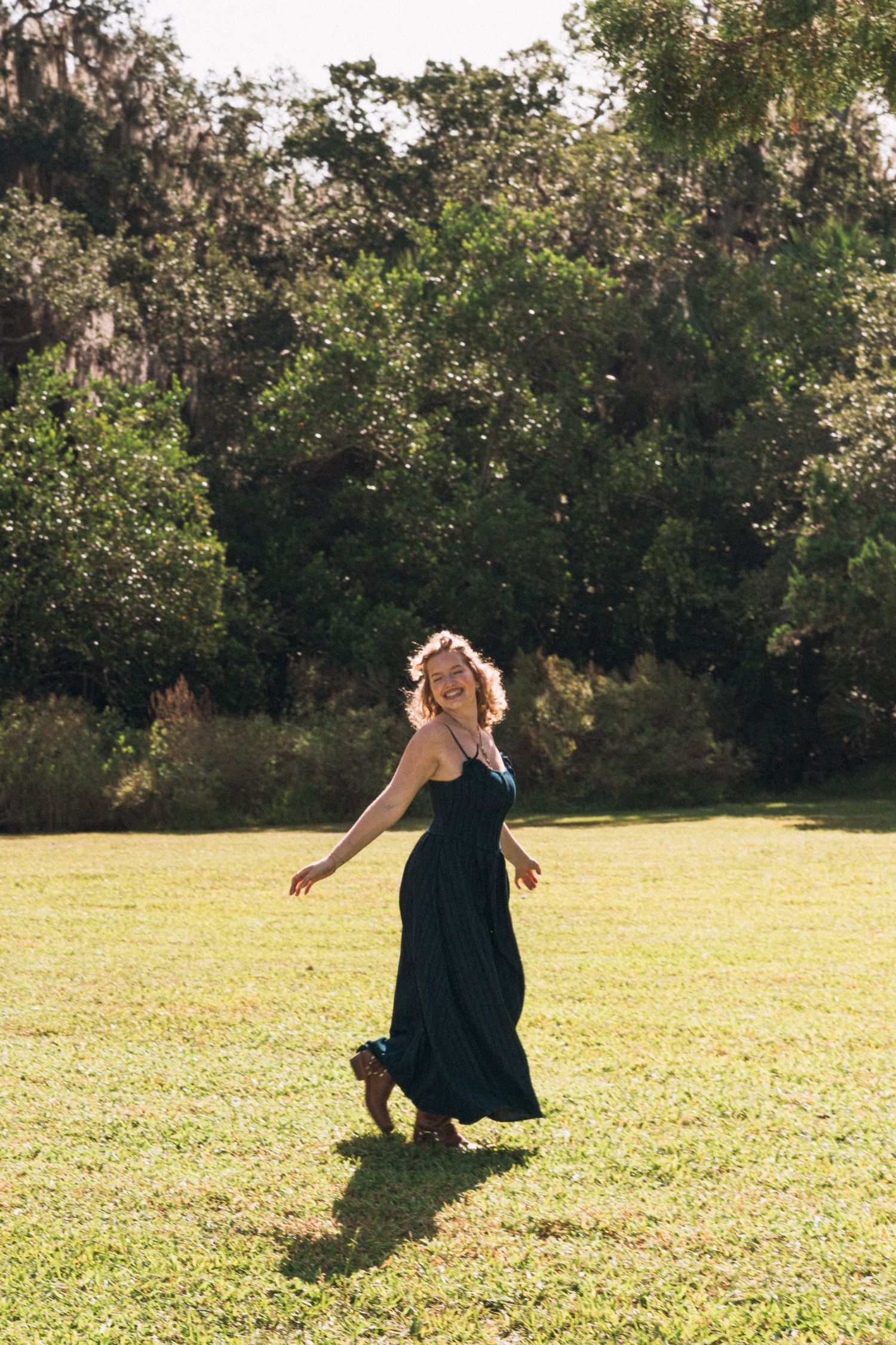 Dancing in a flowing navy dress across a sunlit grassy field.