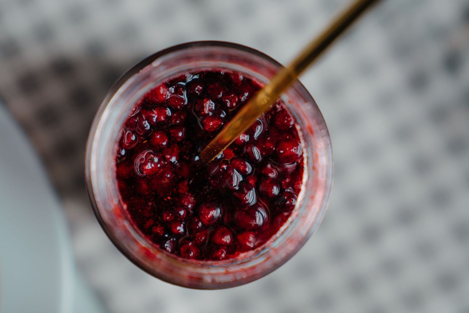 Top view of a refreshing pomegranate drink with seeds and a gold straw in a glass.