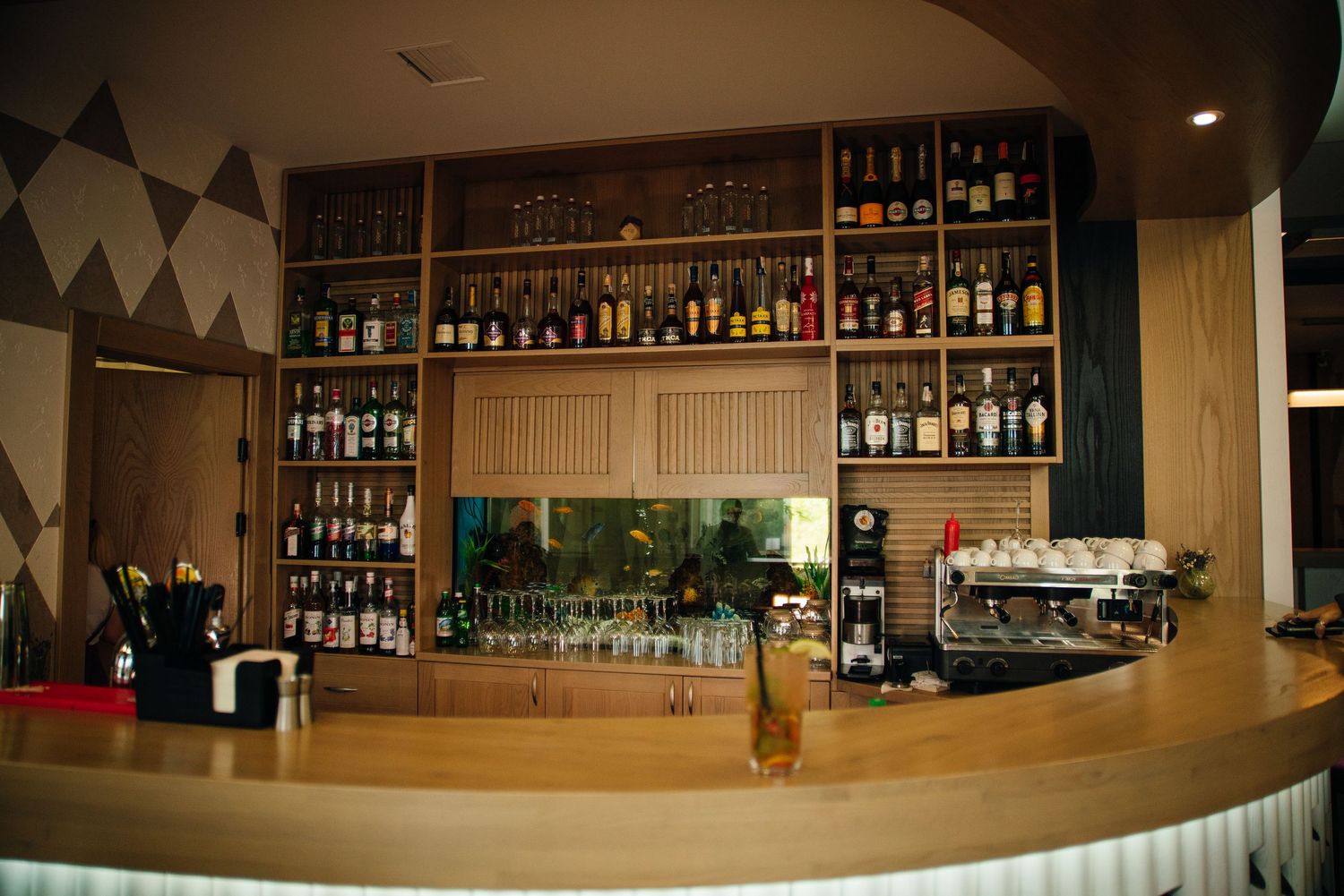 Elegant hotel bar with wooden shelves stocked with bottles and a curved counter.