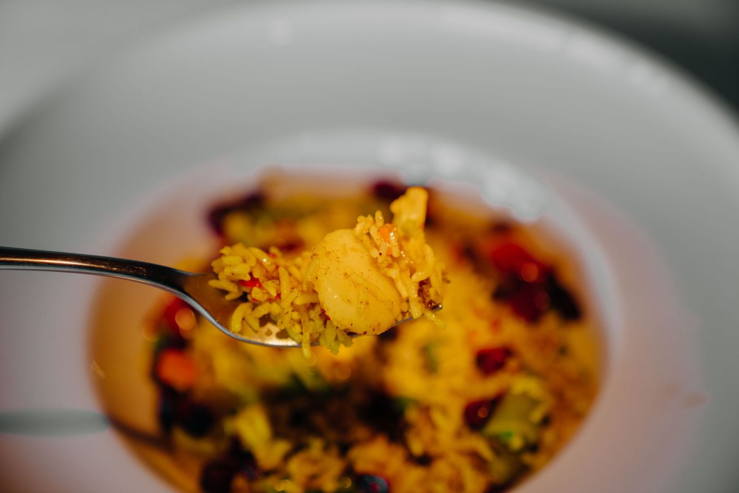 A spoonful of colorful rice dish with turmeric, red pomegranate seeds, and herbs over a white bowl.