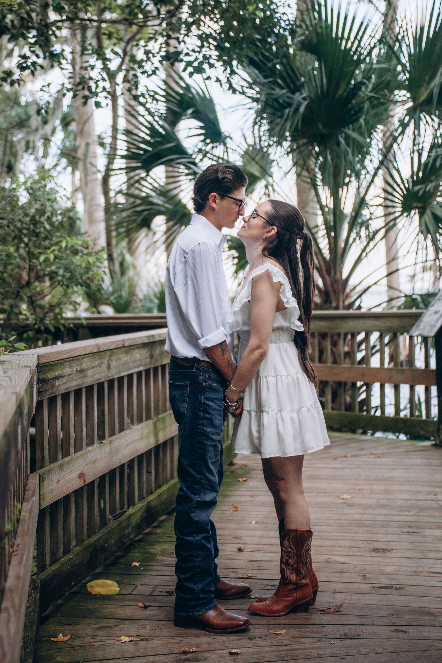 A tender moment captured on a wooden boardwalk surrounded by tropical foliage and palm trees.