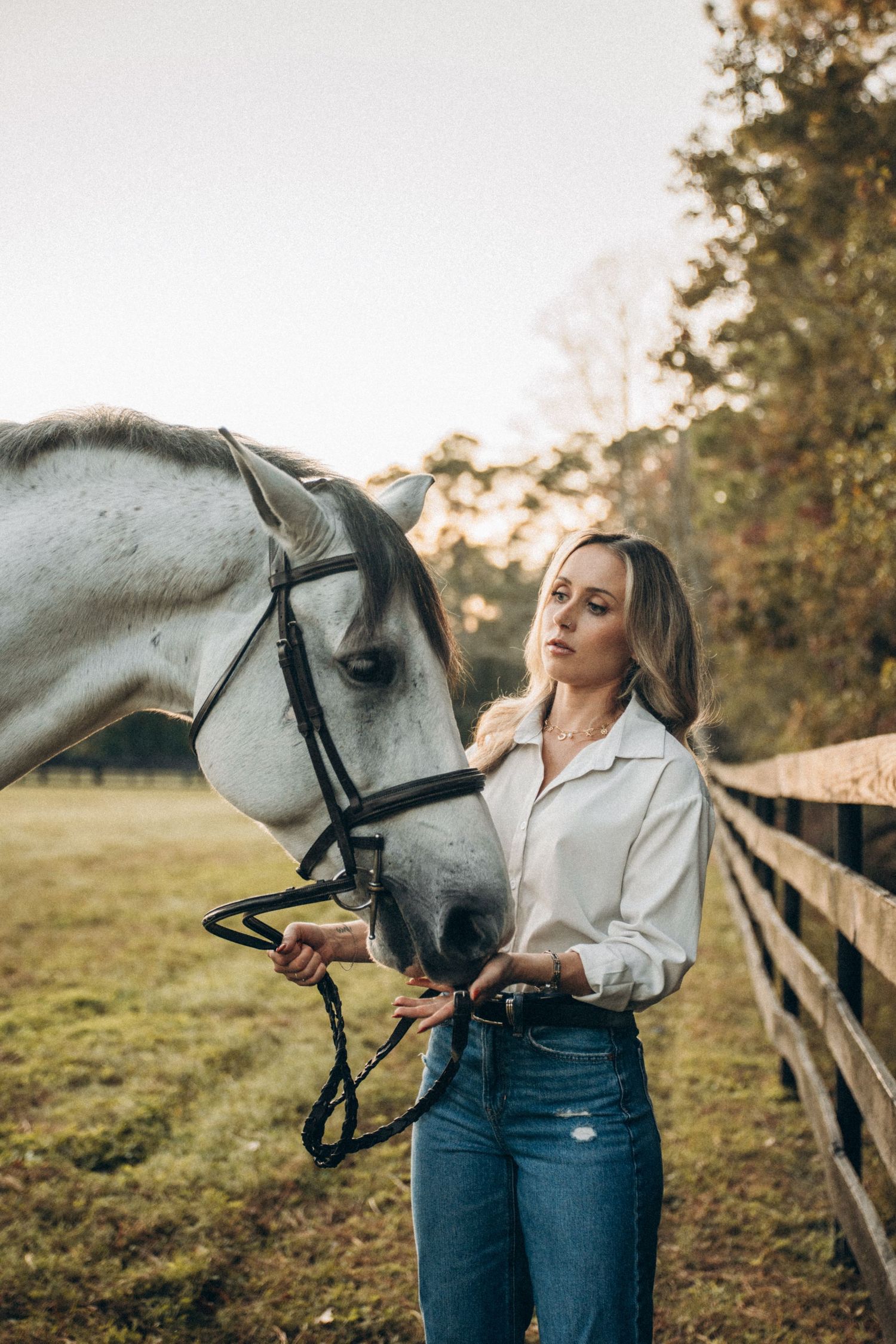 Person in western attire standing with beautiful white horse in pastoral setting at sunset.