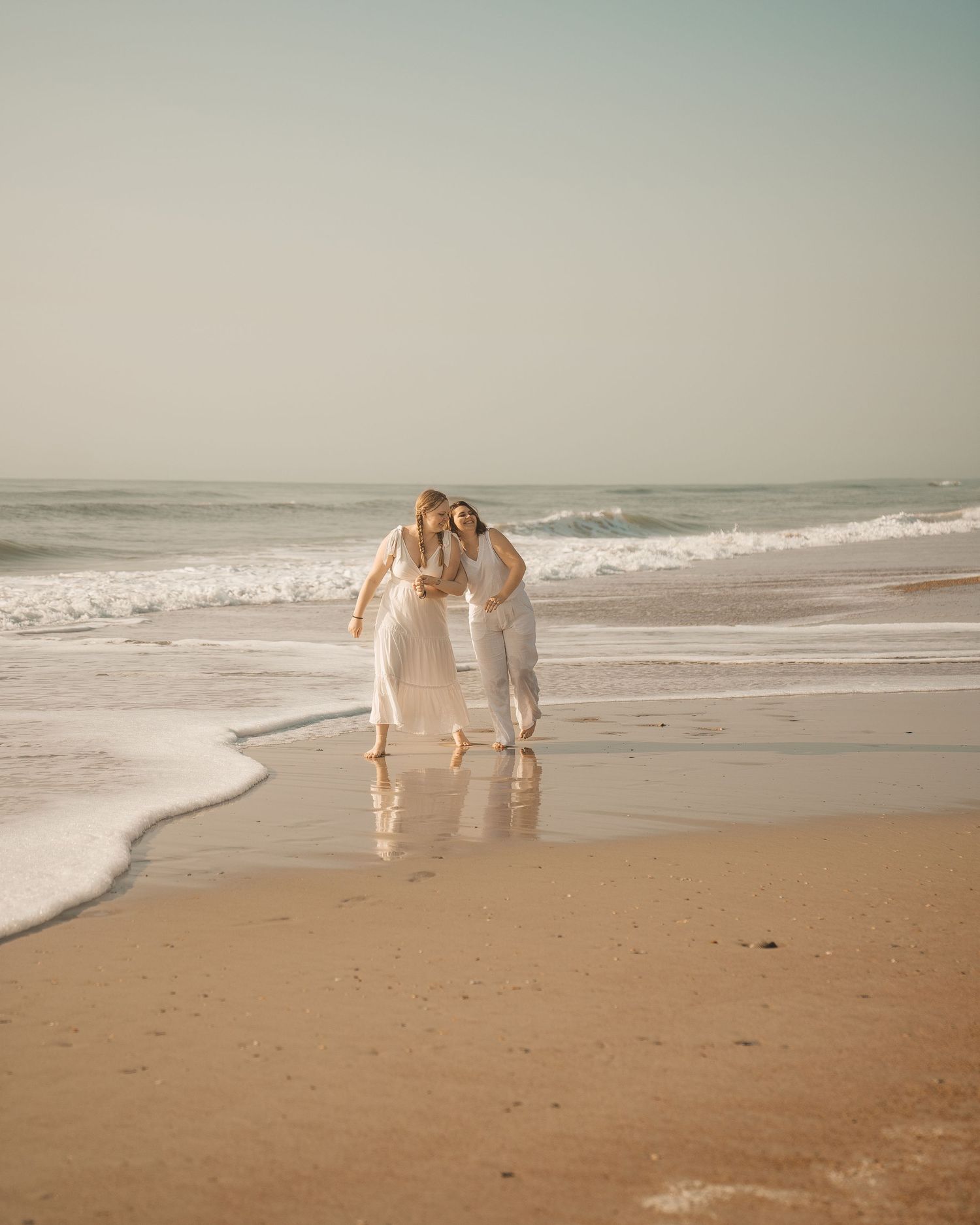 A couple strolls together along the shoreline of a peaceful beach at sunset.