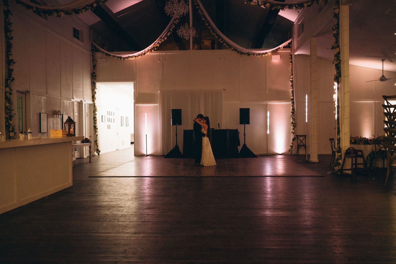 Couple sharing first dance in elegant wedding reception hall with warm uplighting and draped ceiling decor.
