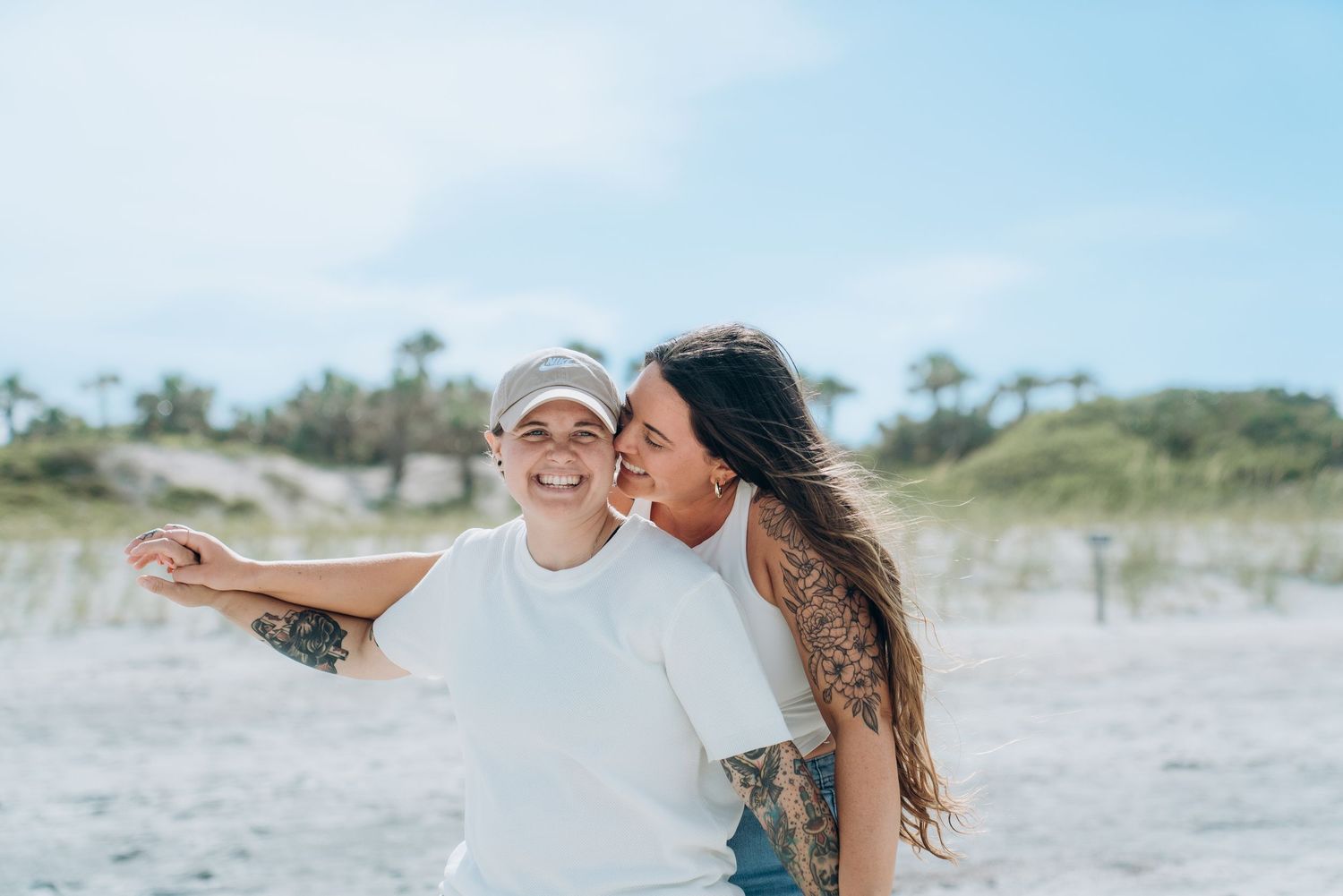 Romantic beach photoshoot with couple dancing in casual outfits against blue sky.