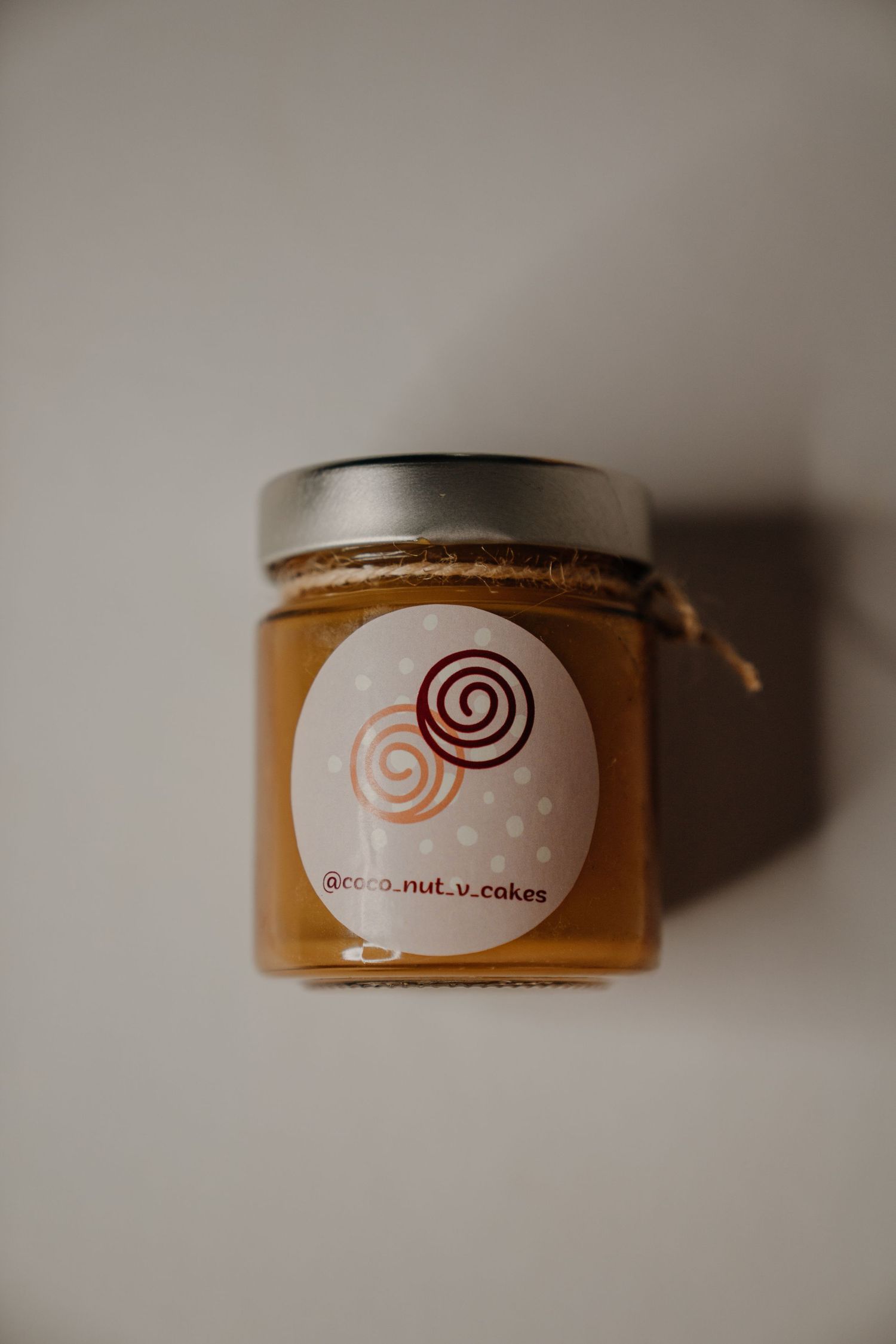 Glass jar of golden honey with a spiral logo label from coco.nut.v.cakes on white background.