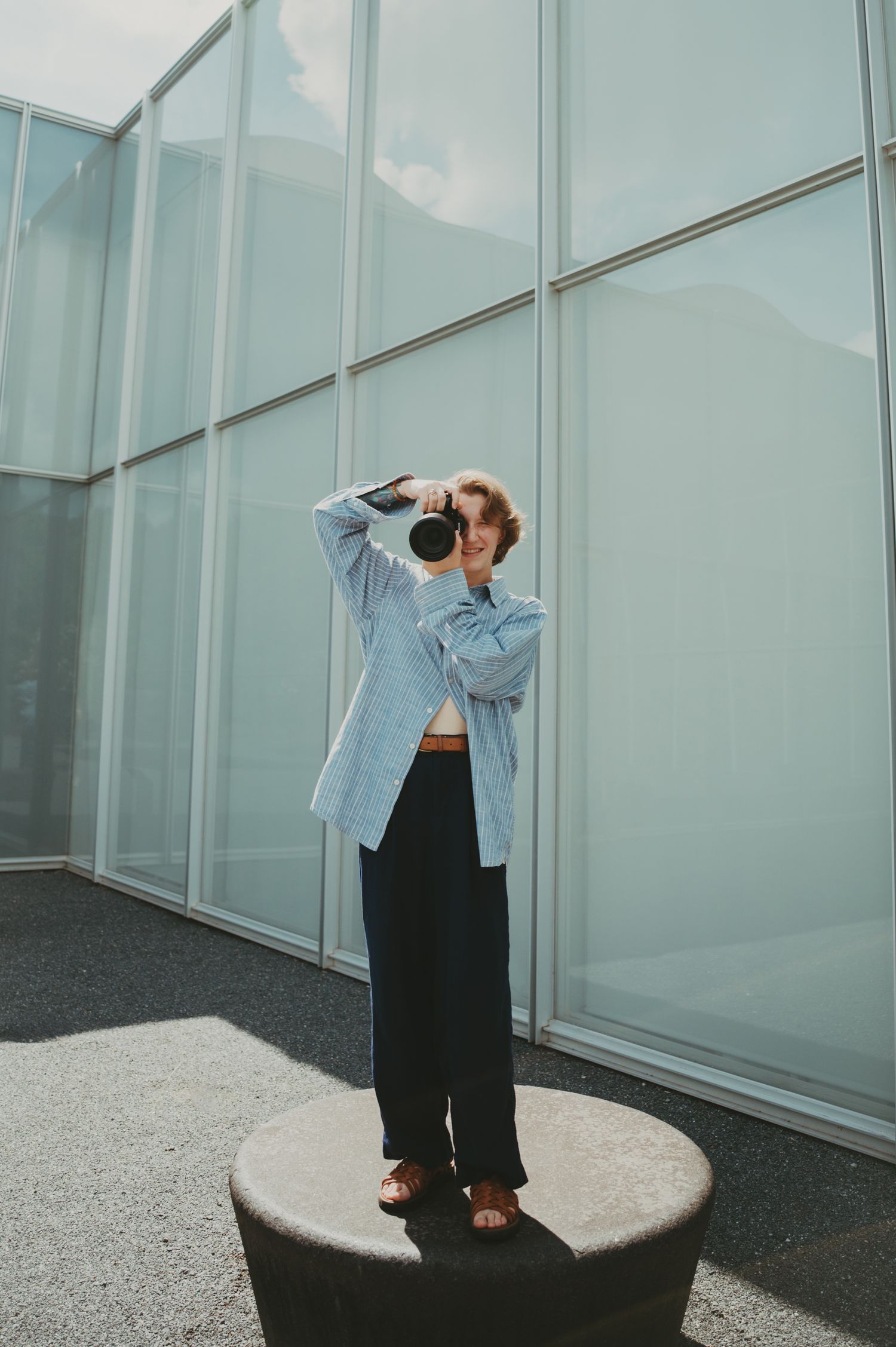 Figure in casual attire photographed against modern glass architecture and blue sky.