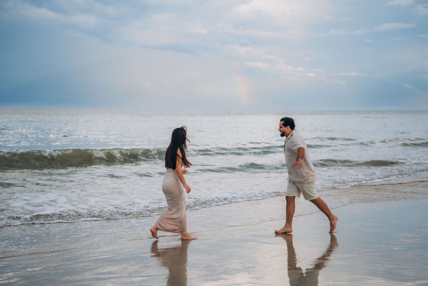 Couple running playfully through the ocean waves on a sunny beach day.