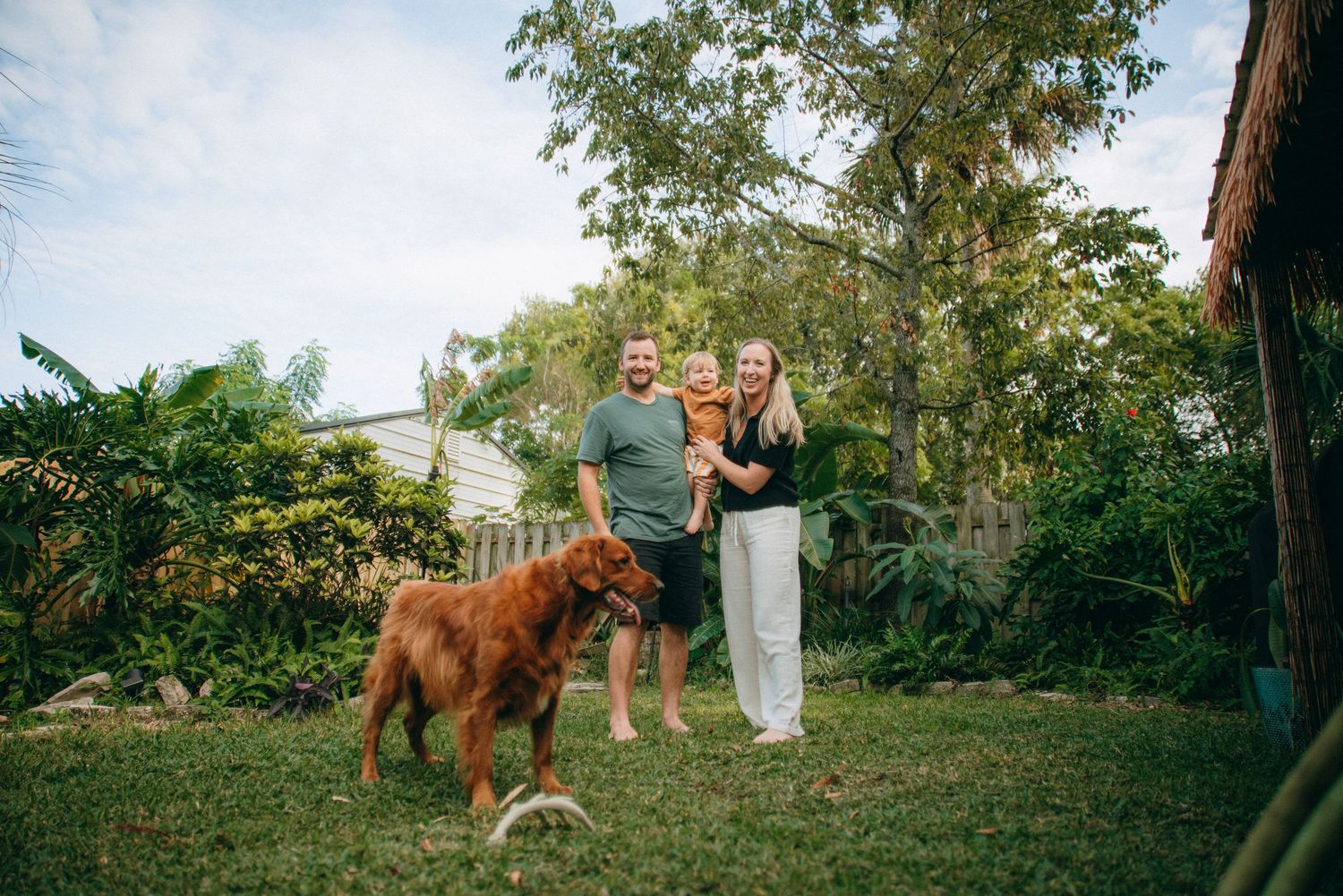 Wide angle view of family and pet dog playing in green backyard space.