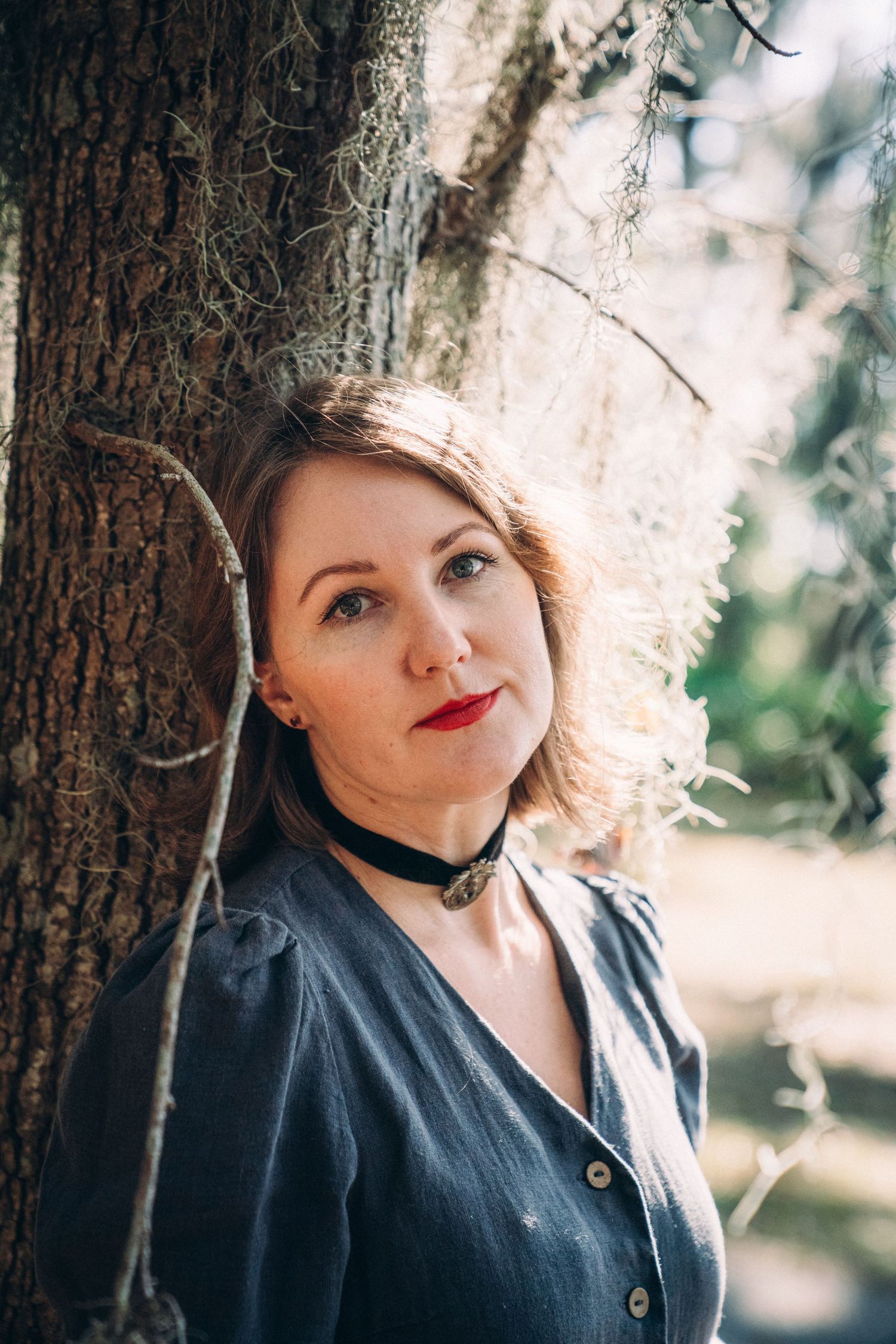 Portrait against a sunlit tree with moss and natural bokeh background.