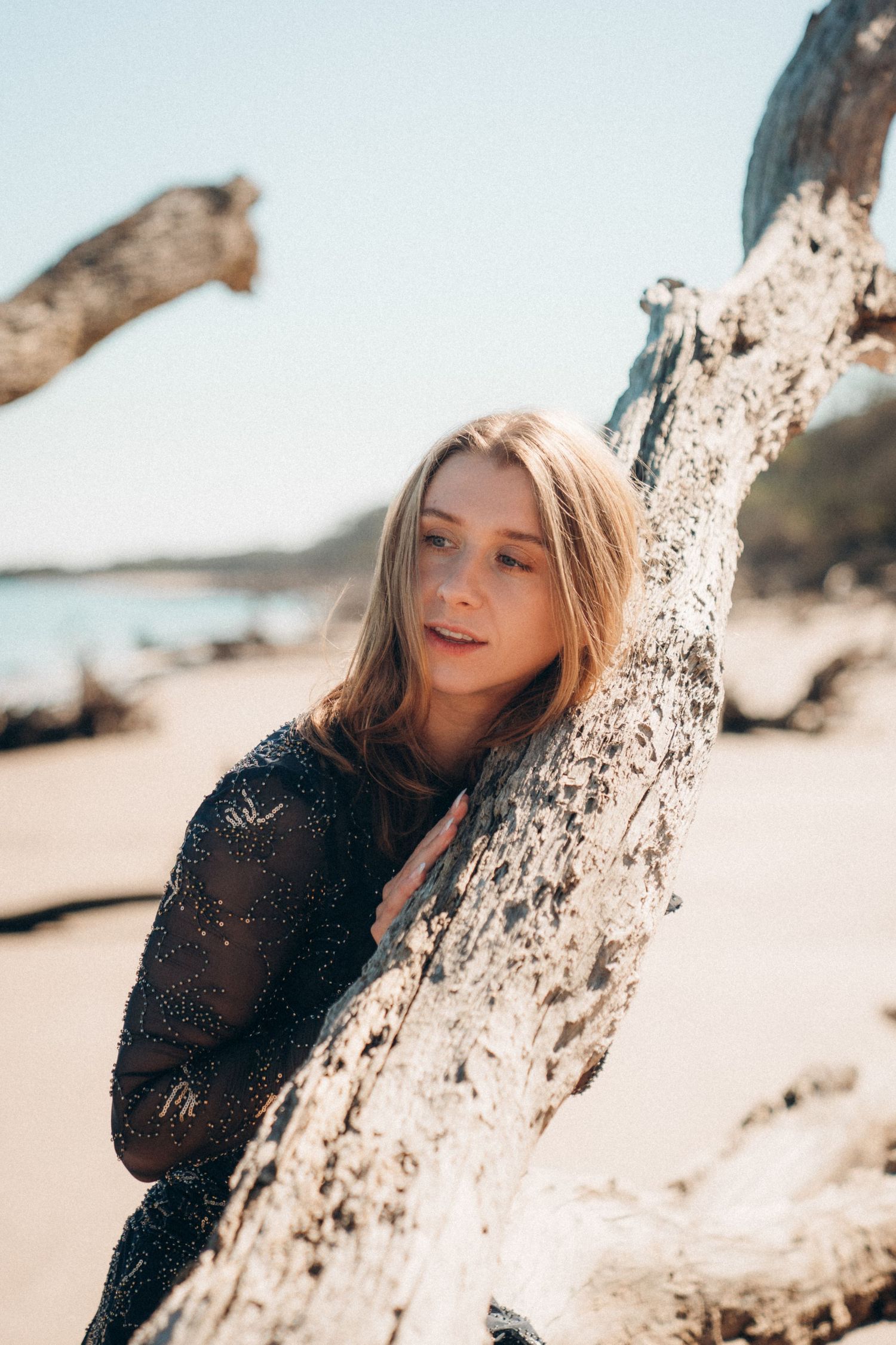 A series of four similar beach portraits showing someone in a black sweater leaning against driftwood in warm sunlight.