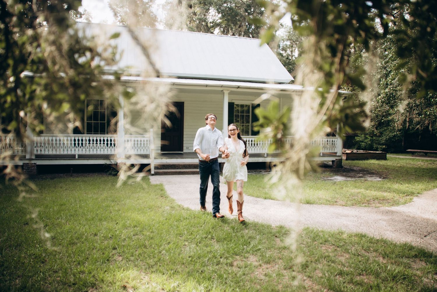 Couple strolls along a winding garden path with lush greenery and a white gazebo in the background.