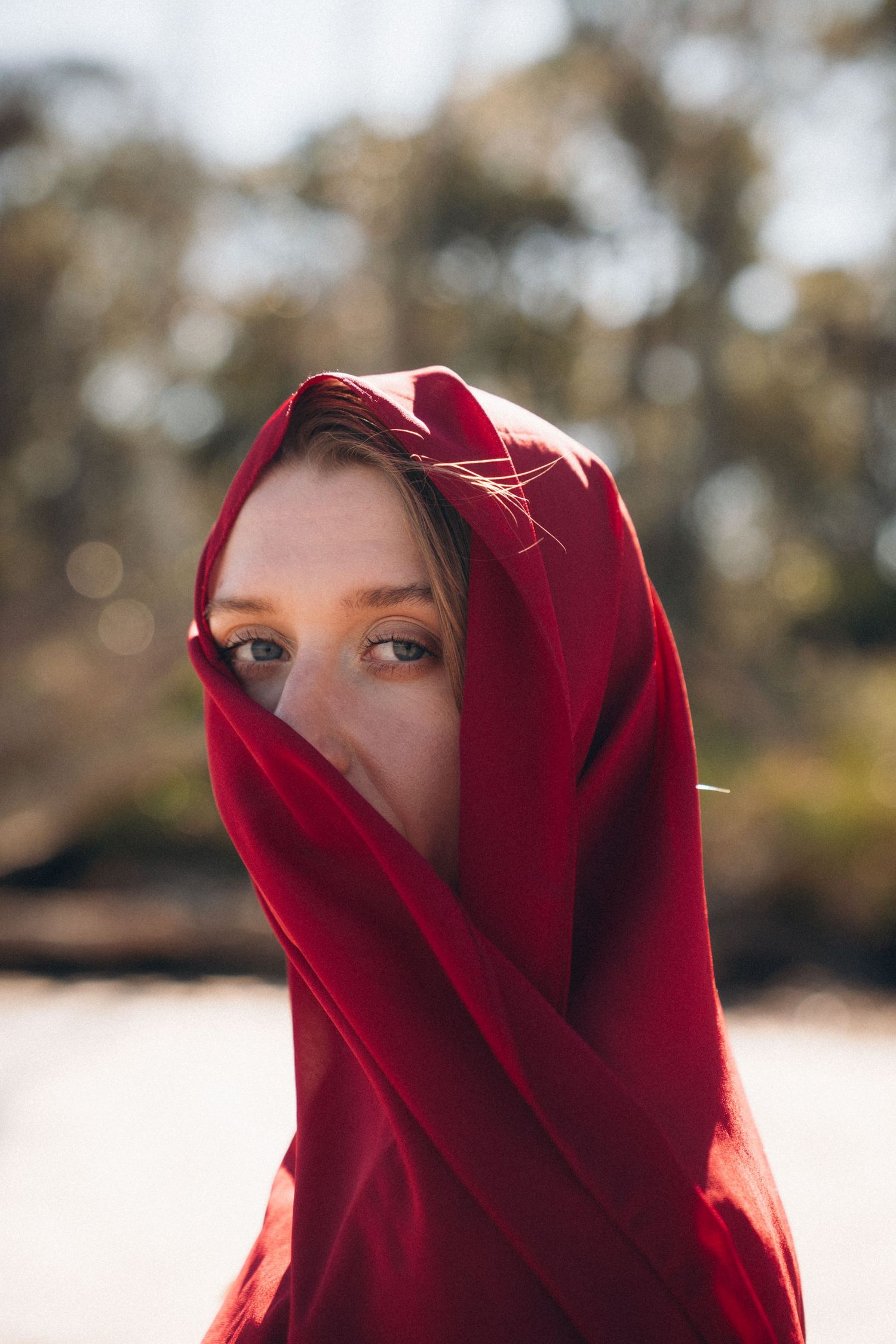 Figure in a deep red hood photographed in soft natural lighting.