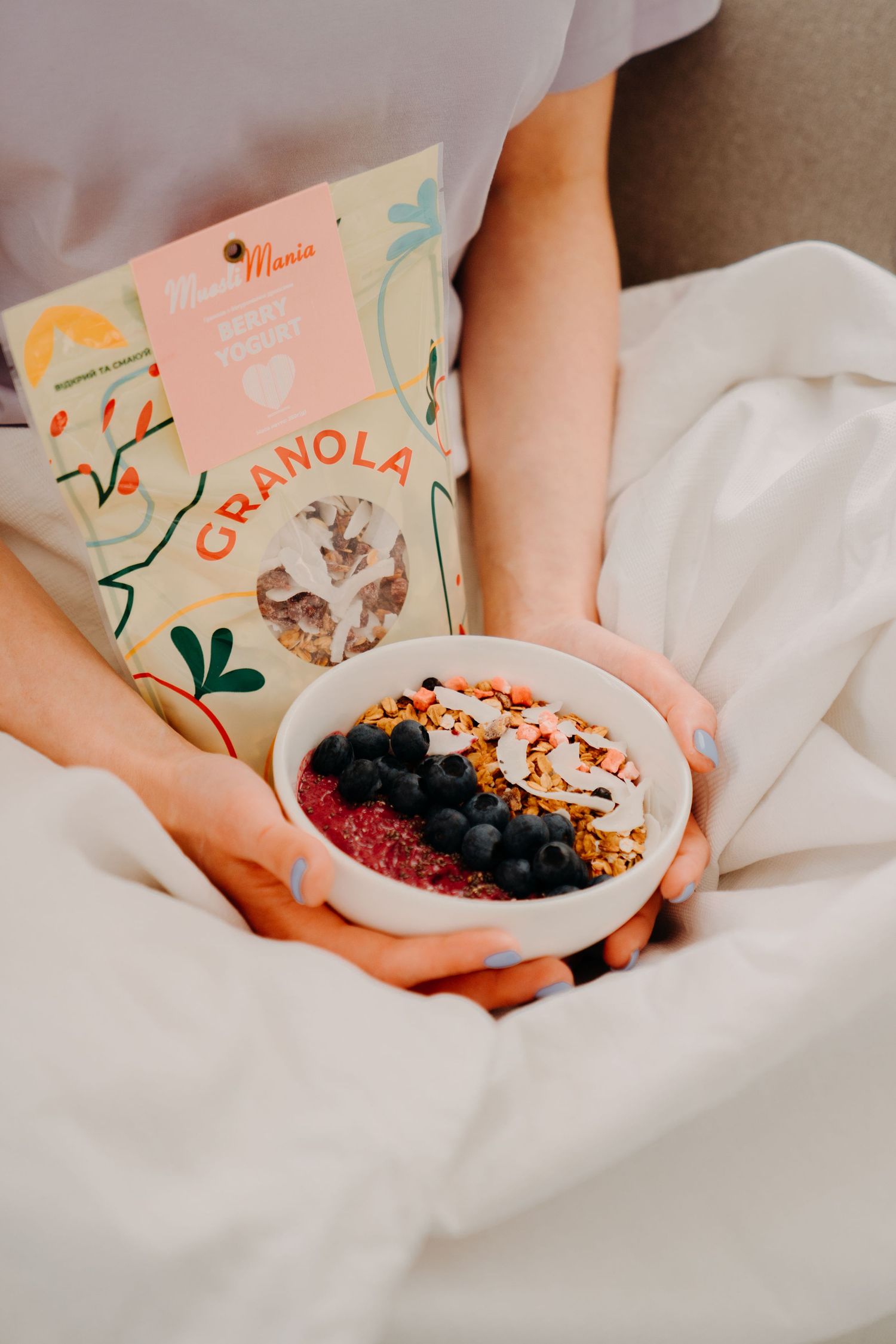 Hands holding a bowl of granola topped with blueberries and a MuesliMania Cranola bag.