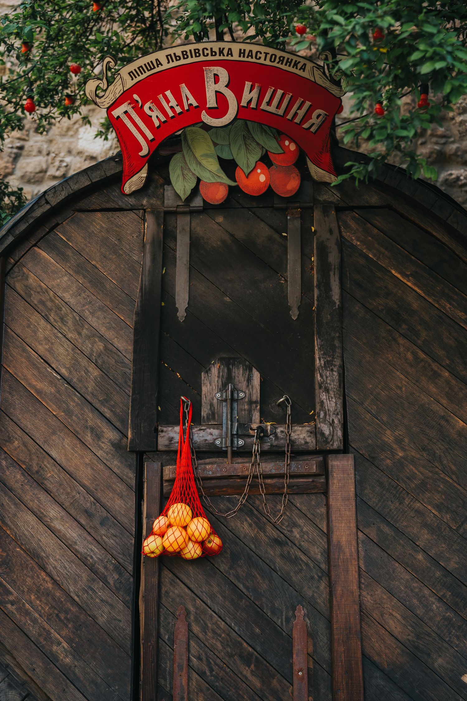 Wooden door of Lviv cherry liquor bar with red sign and hanging net bag of oranges.