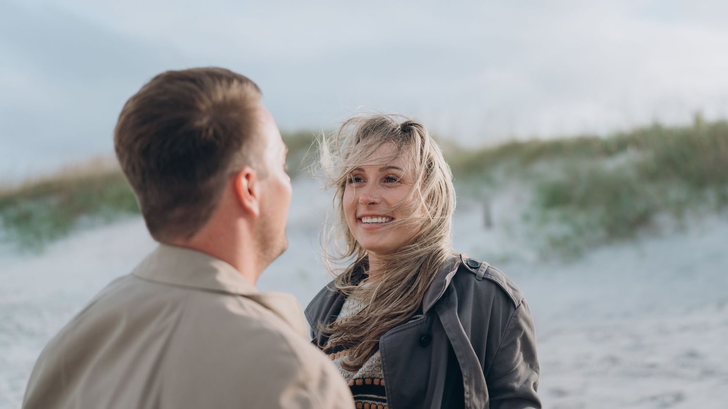 Couple sharing intimate moment on sandy beach with dunes in background.