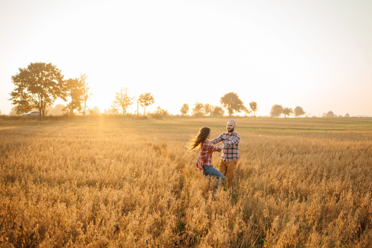 Silhouetted couple dancing in golden wheat field during sunset.