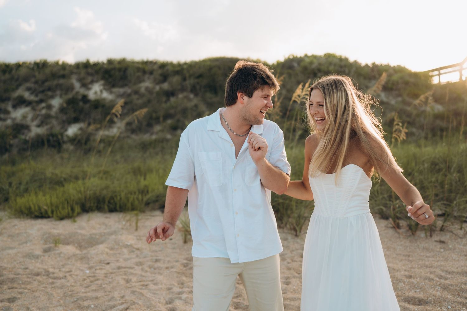Romantic couple in white outfits walking and playing on a beach at sunset.