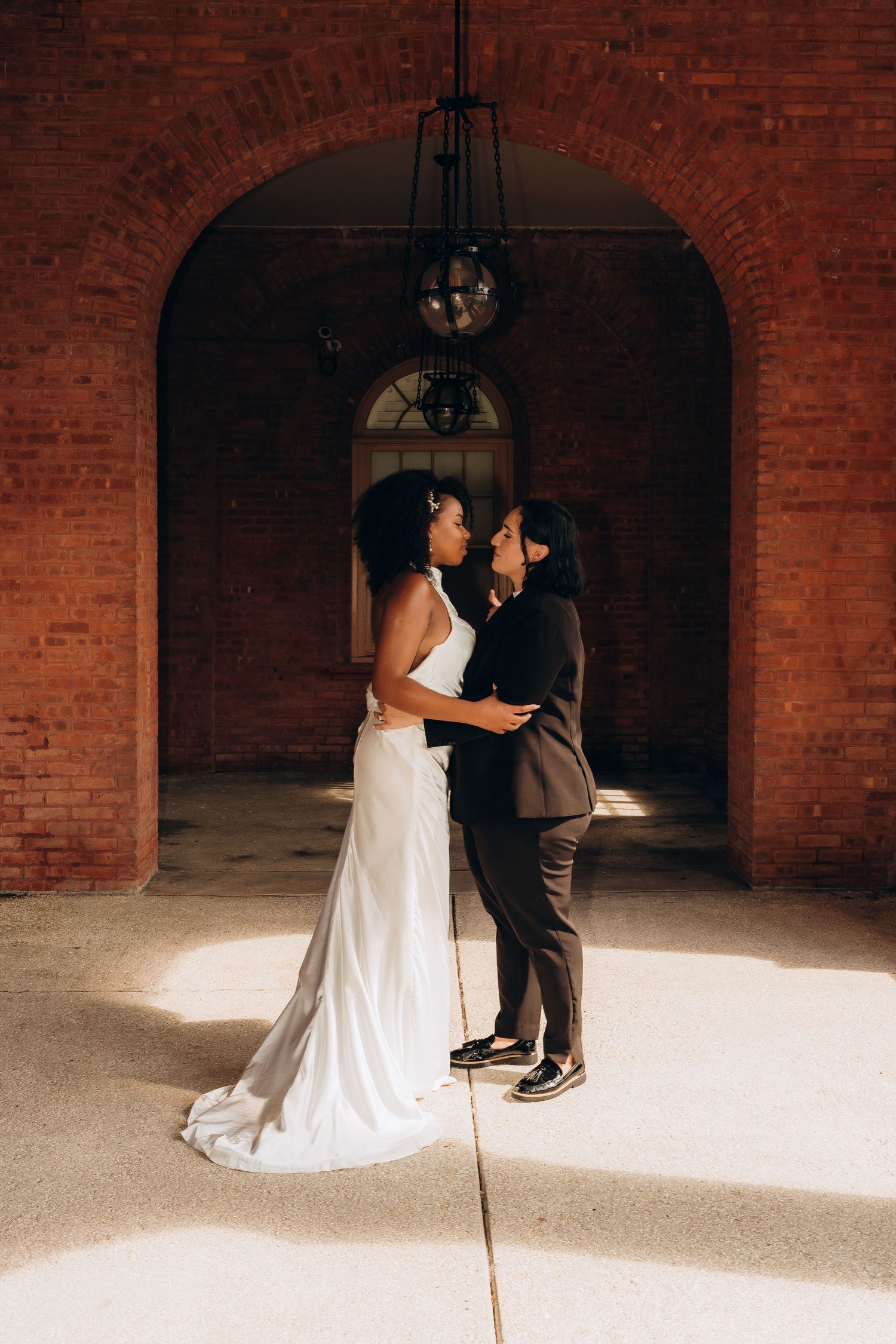 A tender moment between a couple in a brick archway with dramatic natural lighting.