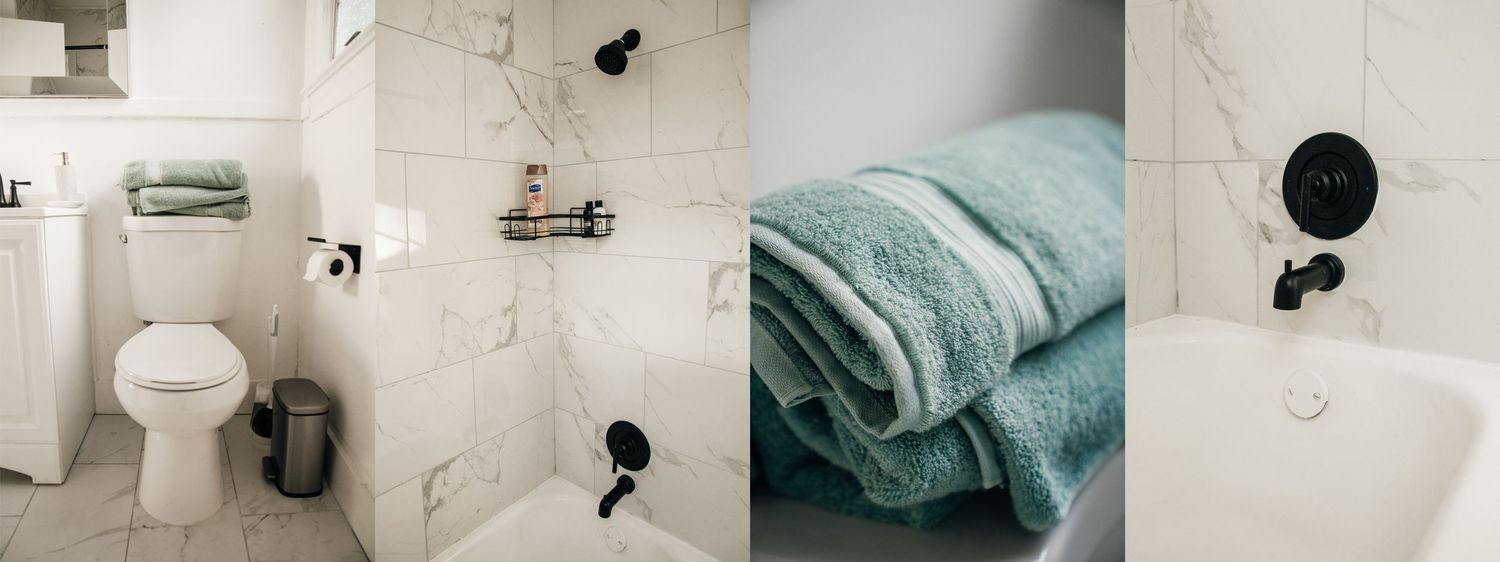 Modern white marble bathroom with toilet, bathtub, black fixtures, and neatly folded teal towels on a shelf.