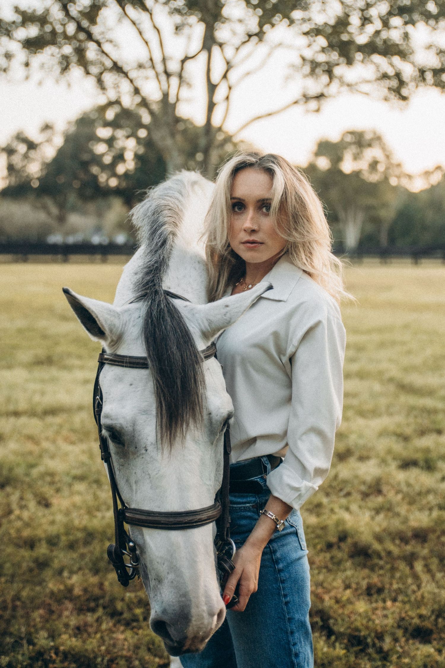 Rustic outdoor portrait session with a white horse against a pastoral background.