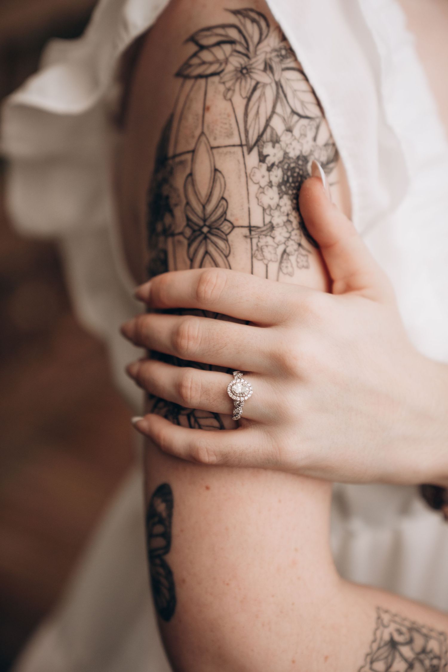 Close-up view of tattooed arm with engagement ring visible.