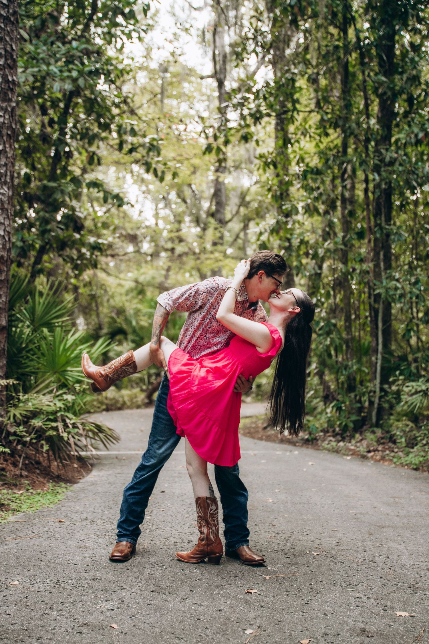 A romantic dip pose on a tree-lined path during an outdoor engagement photoshoot.