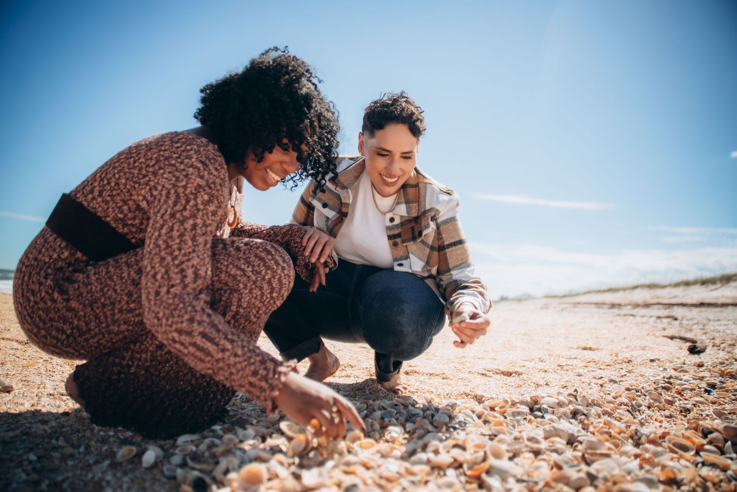 Two people collect seashells together on a sunny beach.
